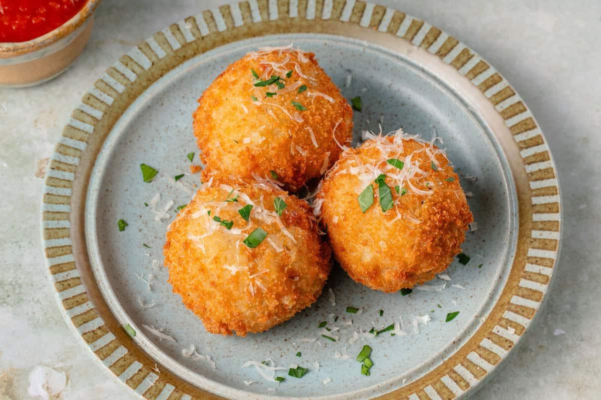 arancini σε μπλε πιάτο με παρμεζάνα και φρέσκο μαϊντανό