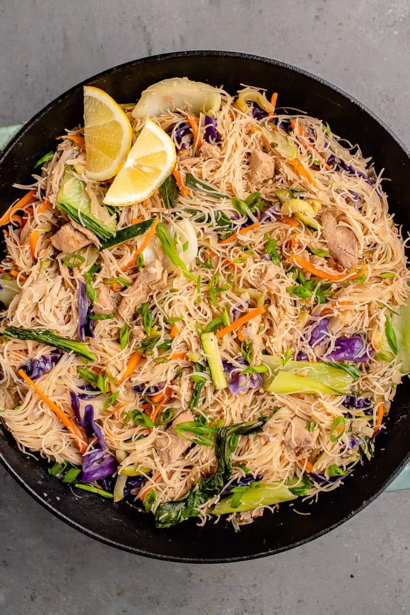 overhead image of vegan filipino pancit bihon with chicken in a wok with lemon