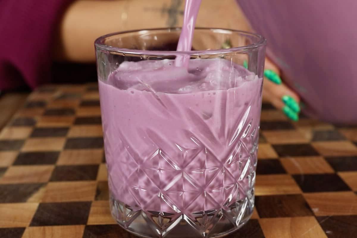 Ούμπε Ορτσάτα (Βίγκαν) 15 pouring ube horchata into glass cup with ice on checker board surface