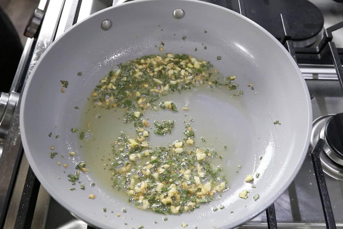Μαγείρεμα ψιλοκομμένου σκόρδου και φασκόμηλου σε βούτυρο σε τηγάνι