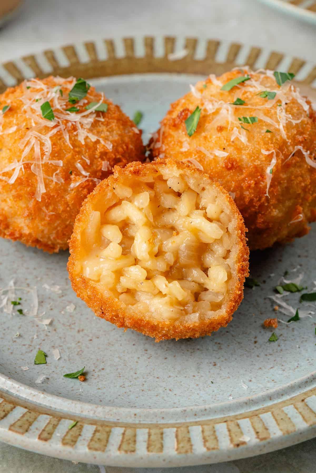 arancini με το εσωτερικό του να φαίνεται σε μπλε πιάτο με παρμεζάνα και φρέσκο μαϊντανό