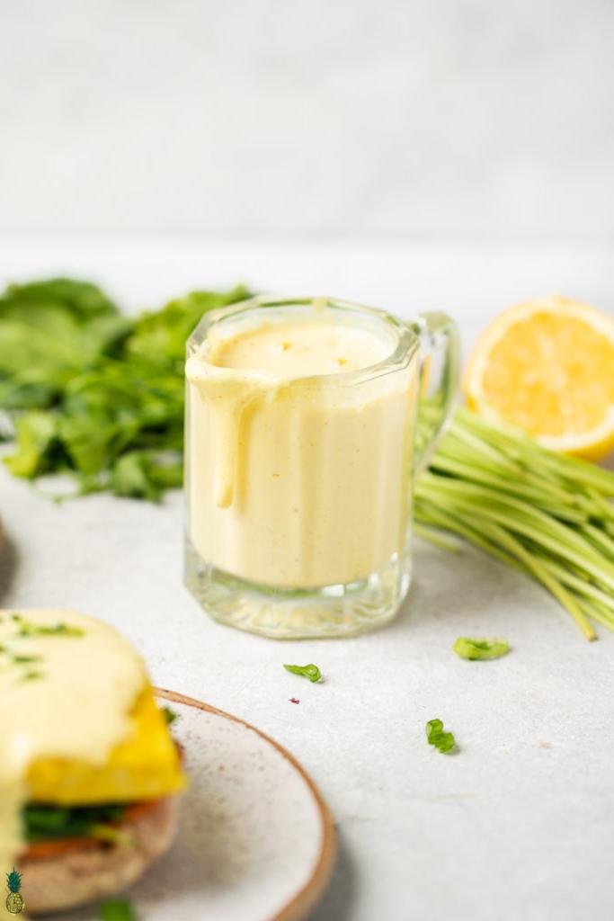 vegan hollandaise sauce in a cup dripping ; lemon, vegan butter, almond milk, nutritional yeast, spices and tofu