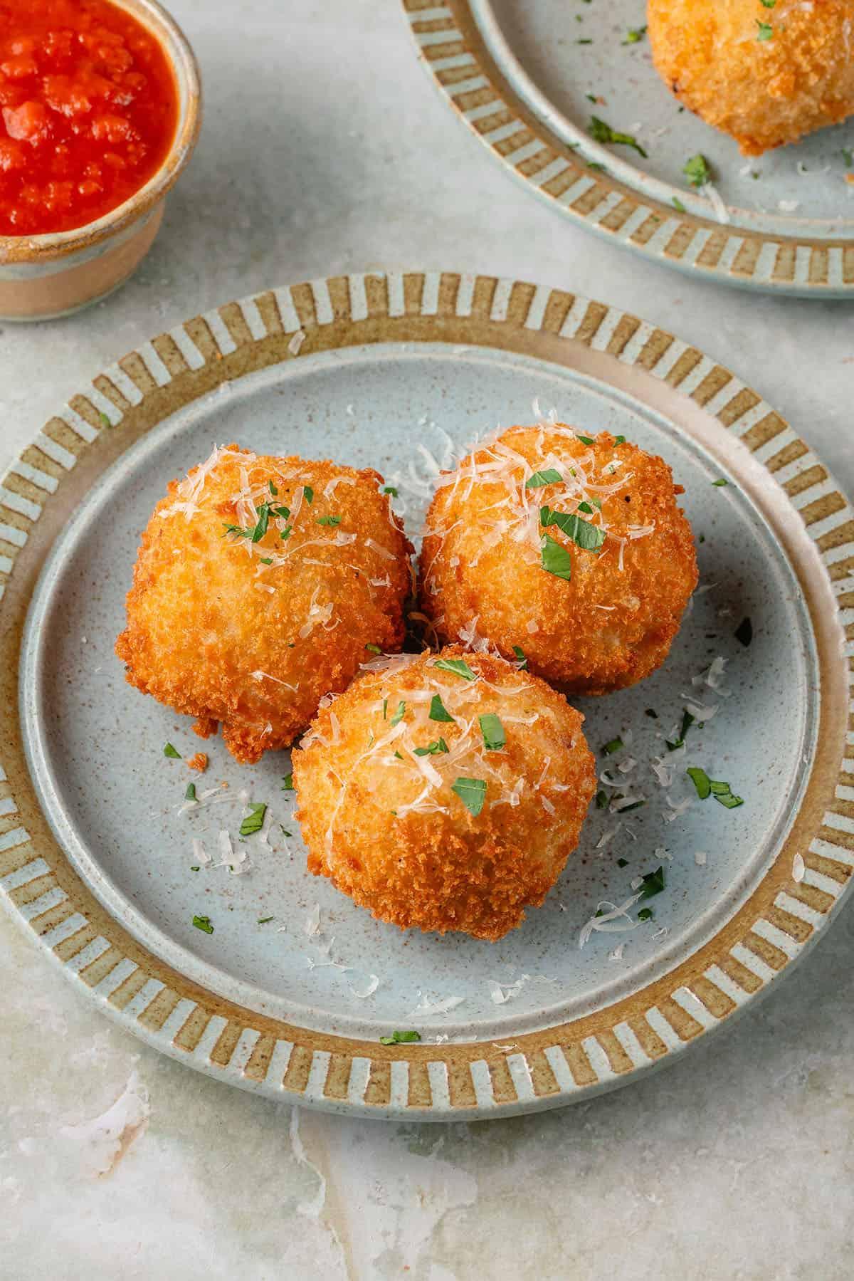 arancini σε μπλε πιάτο με παρμεζάνα και φρέσκο μαϊντανό με μια μερίδα μαρινάρα