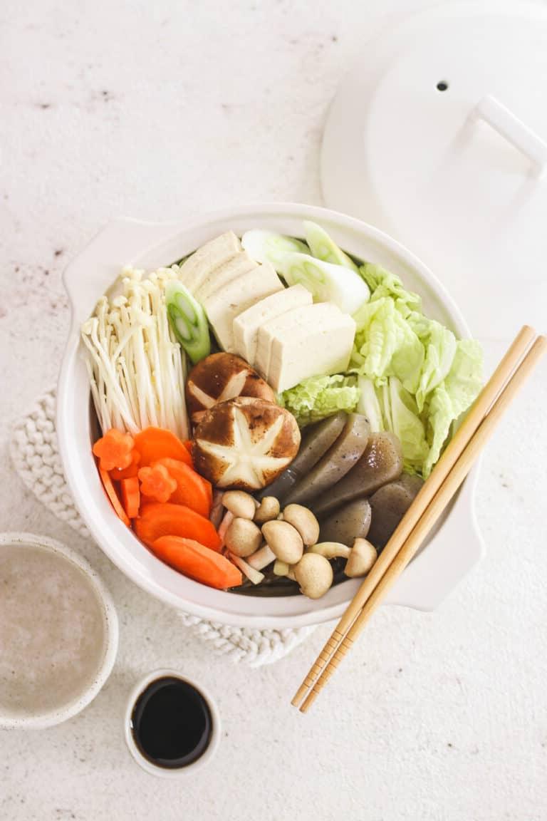 Χορτοφαγικό hot pot σε λευκό μπολ, σε λευκό φόντο με τσοπστικς και σάλτσα σόγιας.