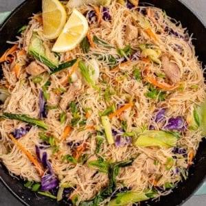 overhead image of vegan filipino pancit bihon with chicken in a wok with lemon