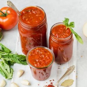 Σπιτική σάλτσα μαρινάρα σε βάζα με τα υλικά και λευκό φόντο