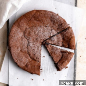 A large slice of Flourless Chocolate Espresso Cake, dusted with powdered sugar and topped with whipped cream, on a plate.