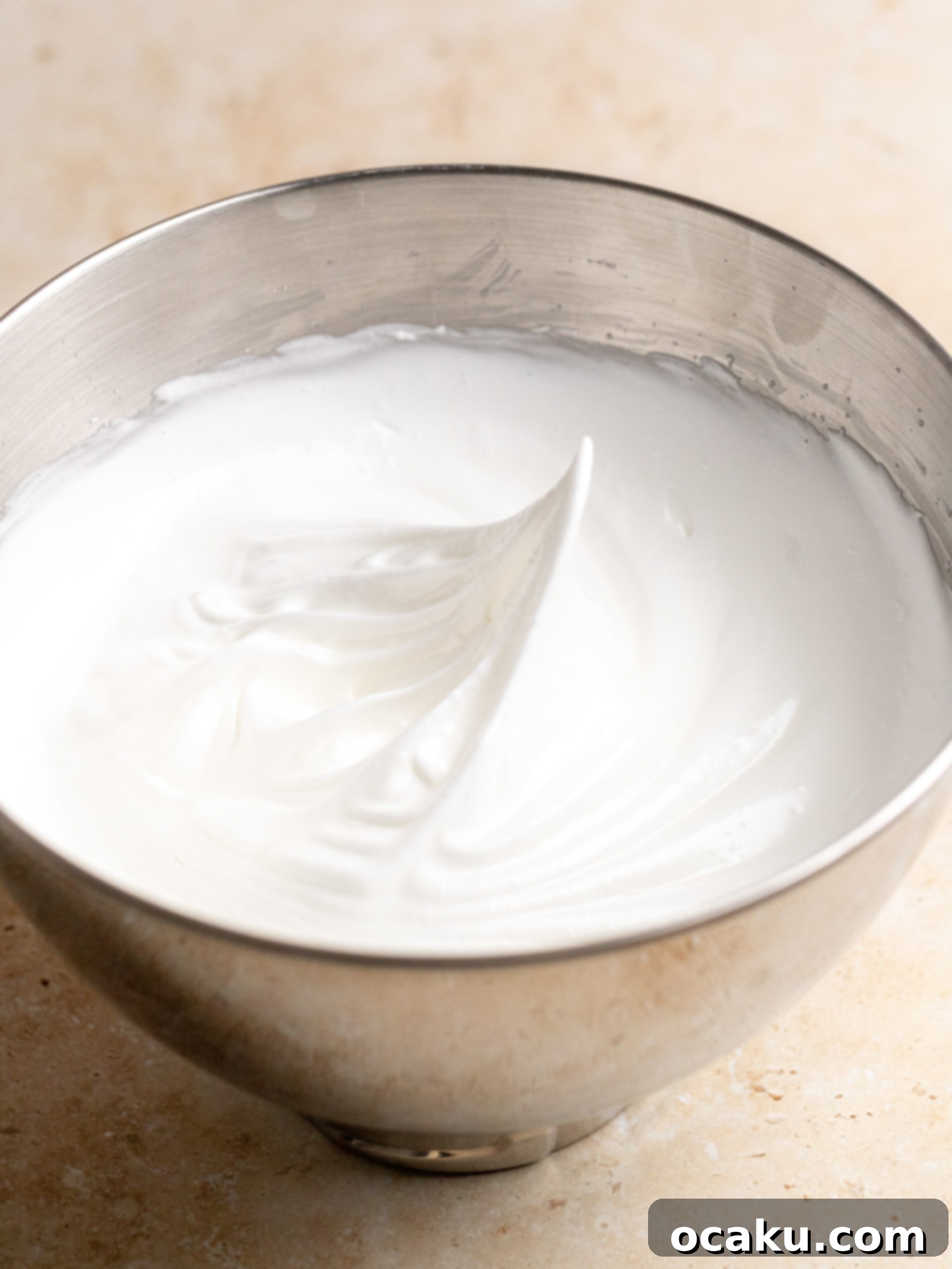 Granulated sugar being gradually added to frothy egg whites during meringue preparation.