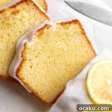 A beautifully glazed lemon loaf cake, topped with fresh lemon slices, captured from above.