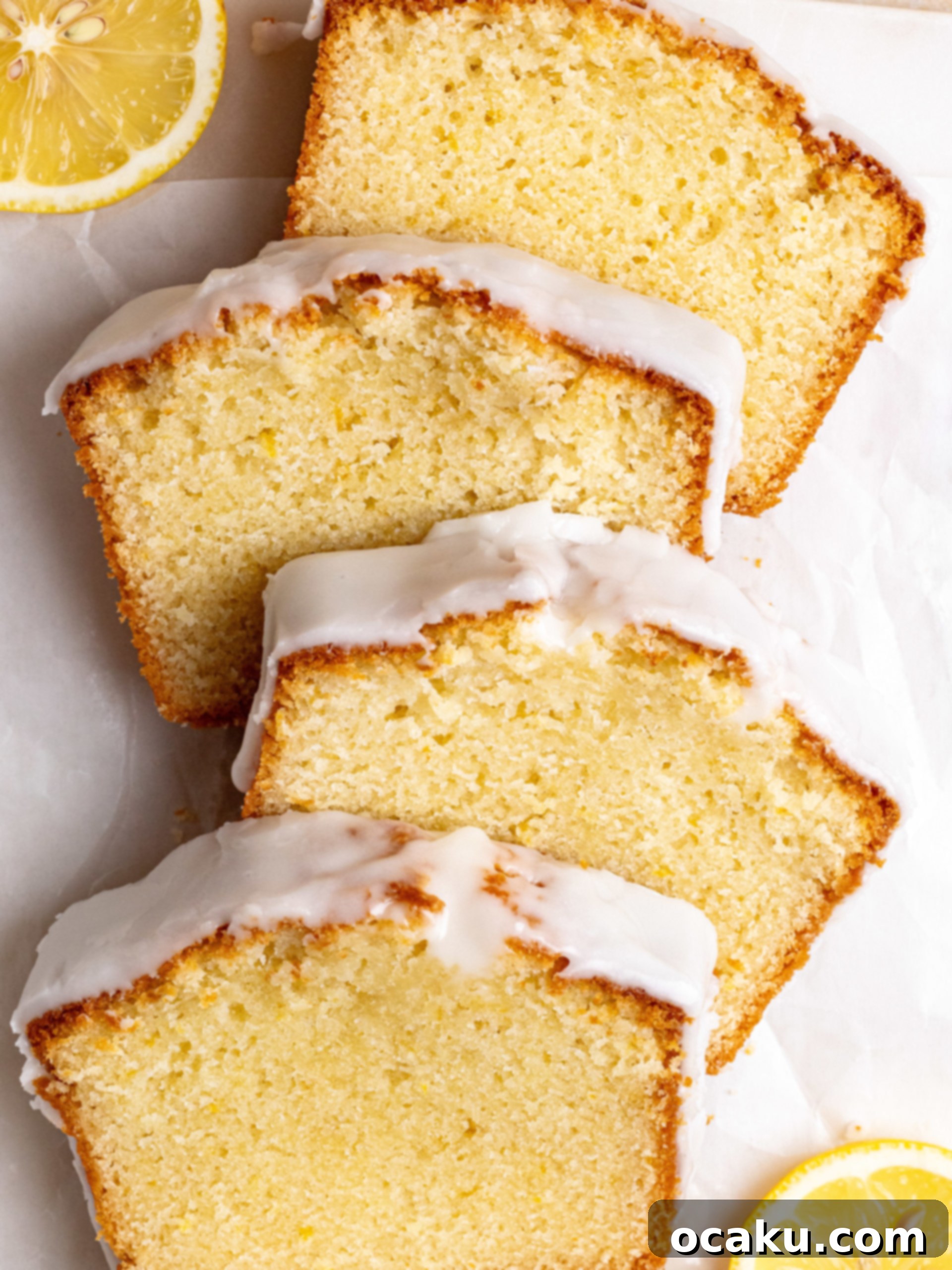 Two slices of lemon loaf cake, one with a bite taken, showcasing the moist interior and thick lemon glaze, on a white plate with lemon wedges.