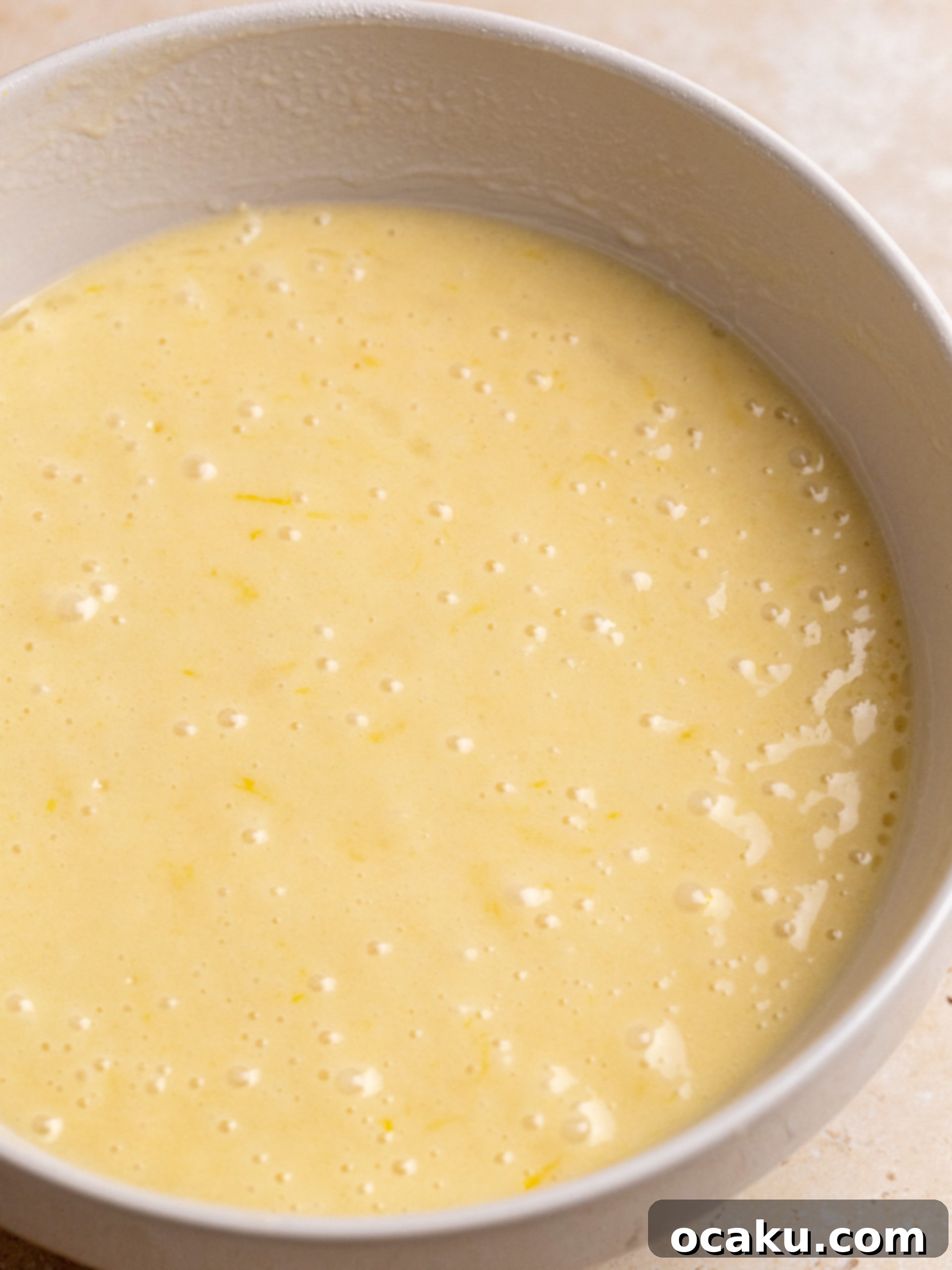 Close-up of lemon loaf cake batter in a loaf pan before baking, with a knife creating a furrow down the middle.