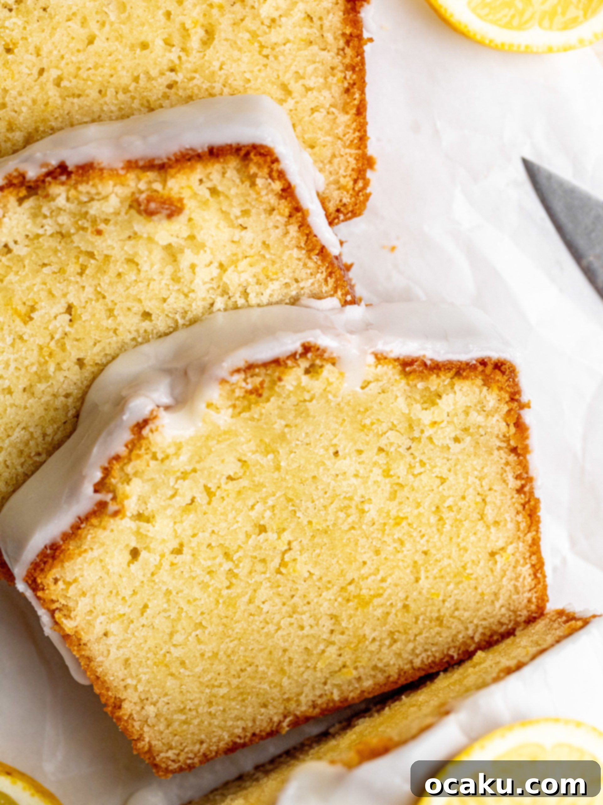 A beautiful lemon loaf cake with a thick, white glaze, decorated with fresh lemon slices, on a wooden board.