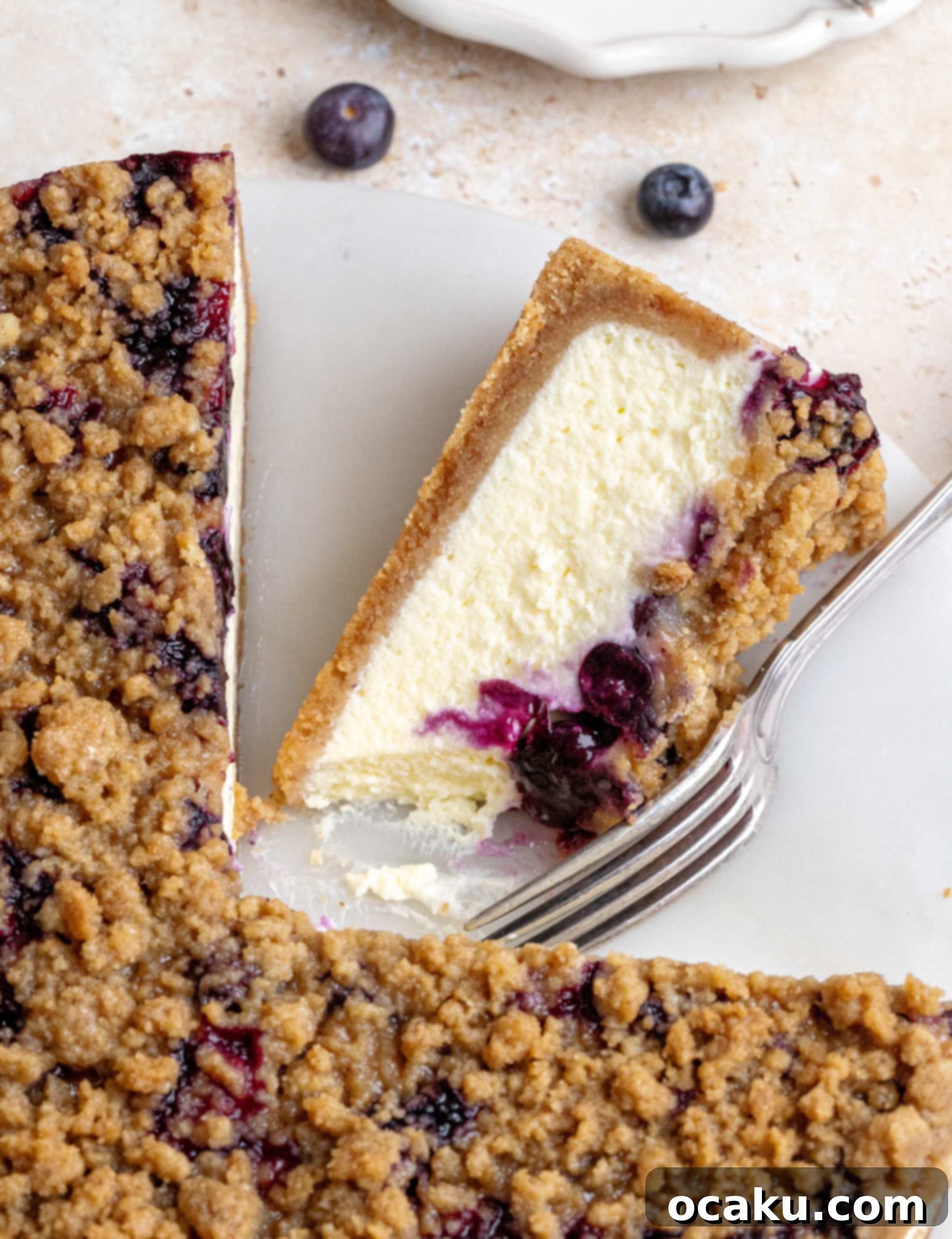A whole blueberry crumble cheesecake on a serving platter, showcasing its vibrant blueberry and crumble topping, ready to be sliced.