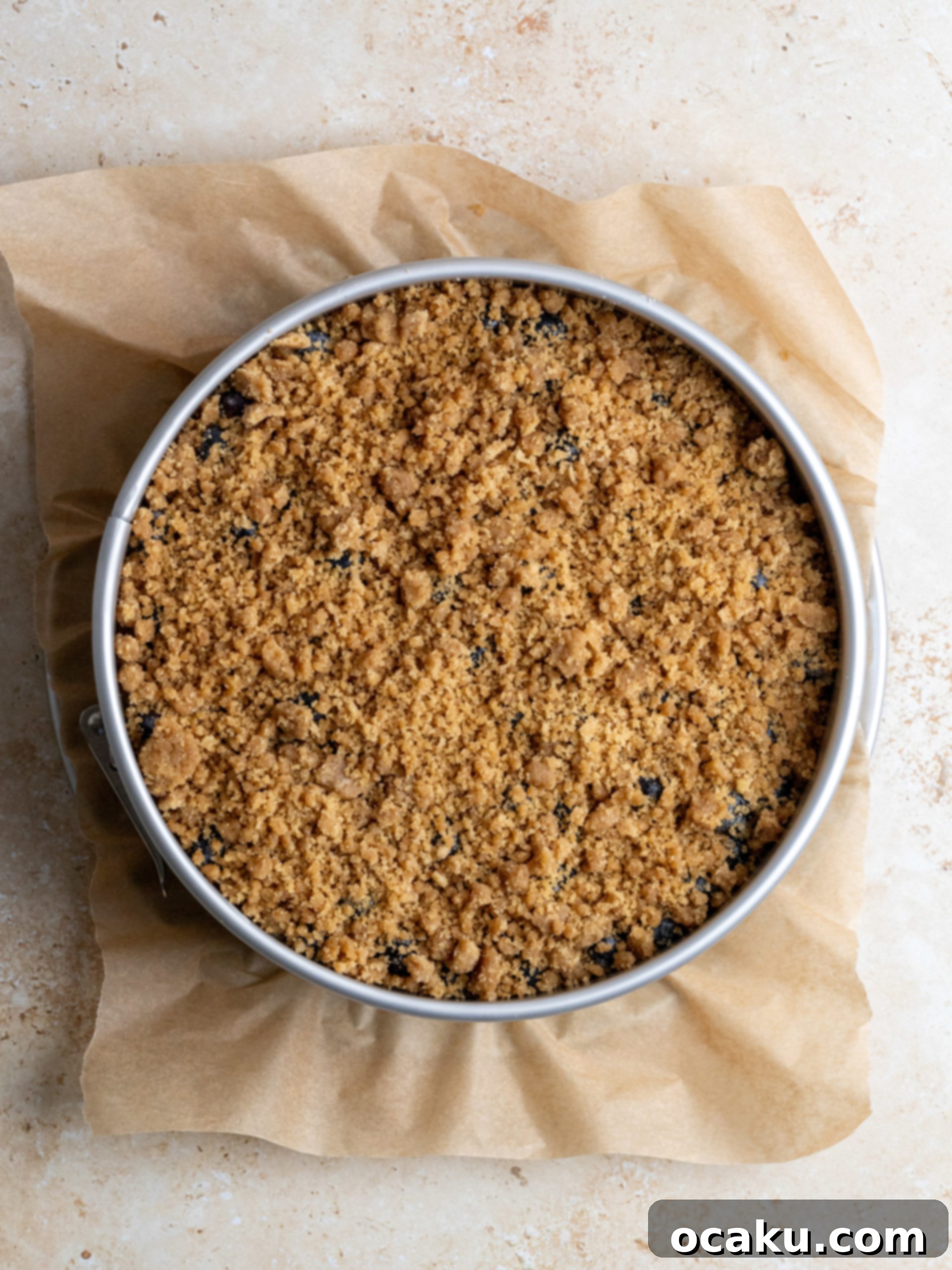 Crumble topping being sprinkled over the blueberries on the cheesecake.