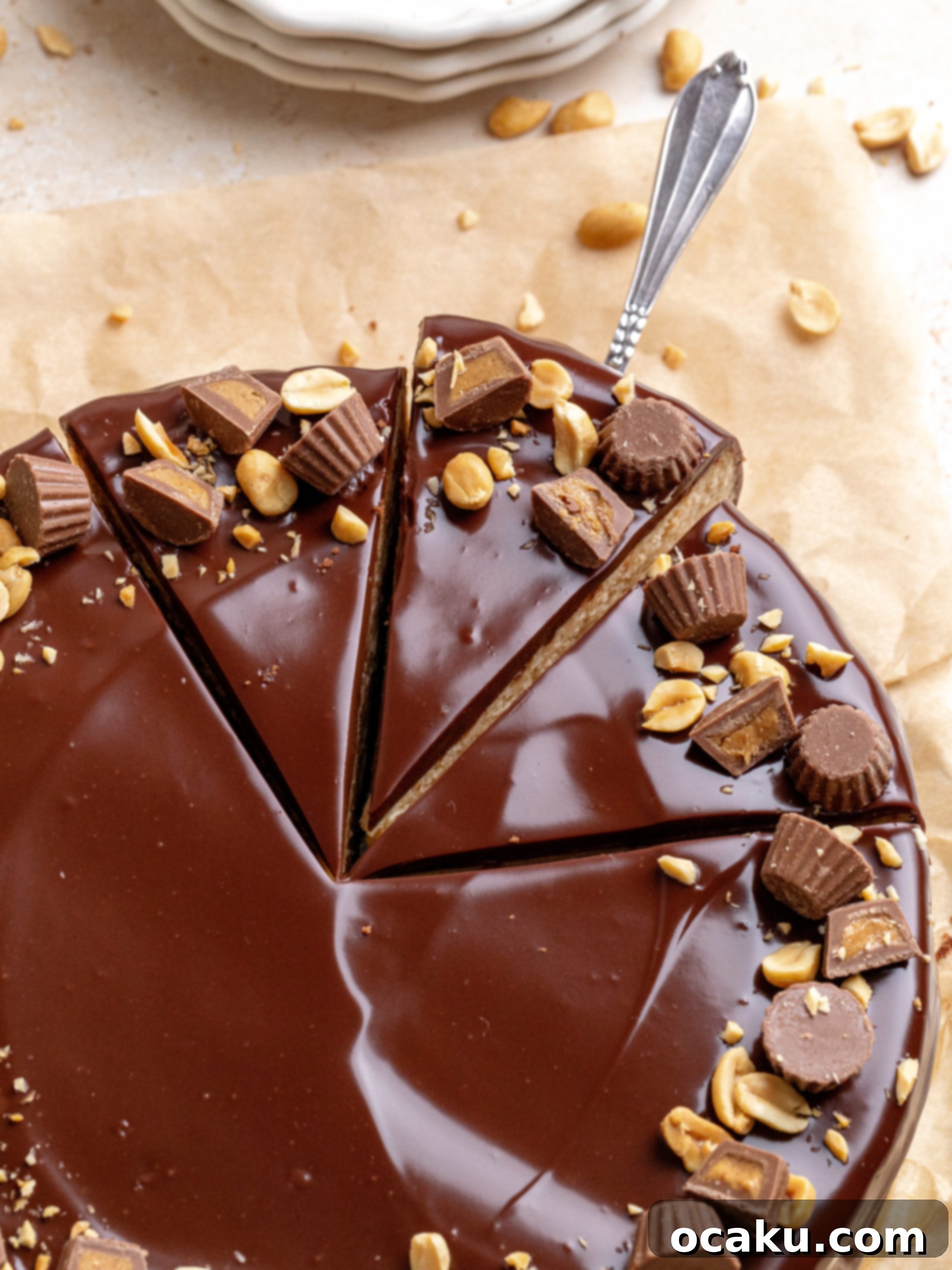 A beautifully sliced piece of Peanut Butter Chocolate Cheesecake on a white plate, garnished with a mini Reese's cup and peanuts, with a full cheesecake in the background.