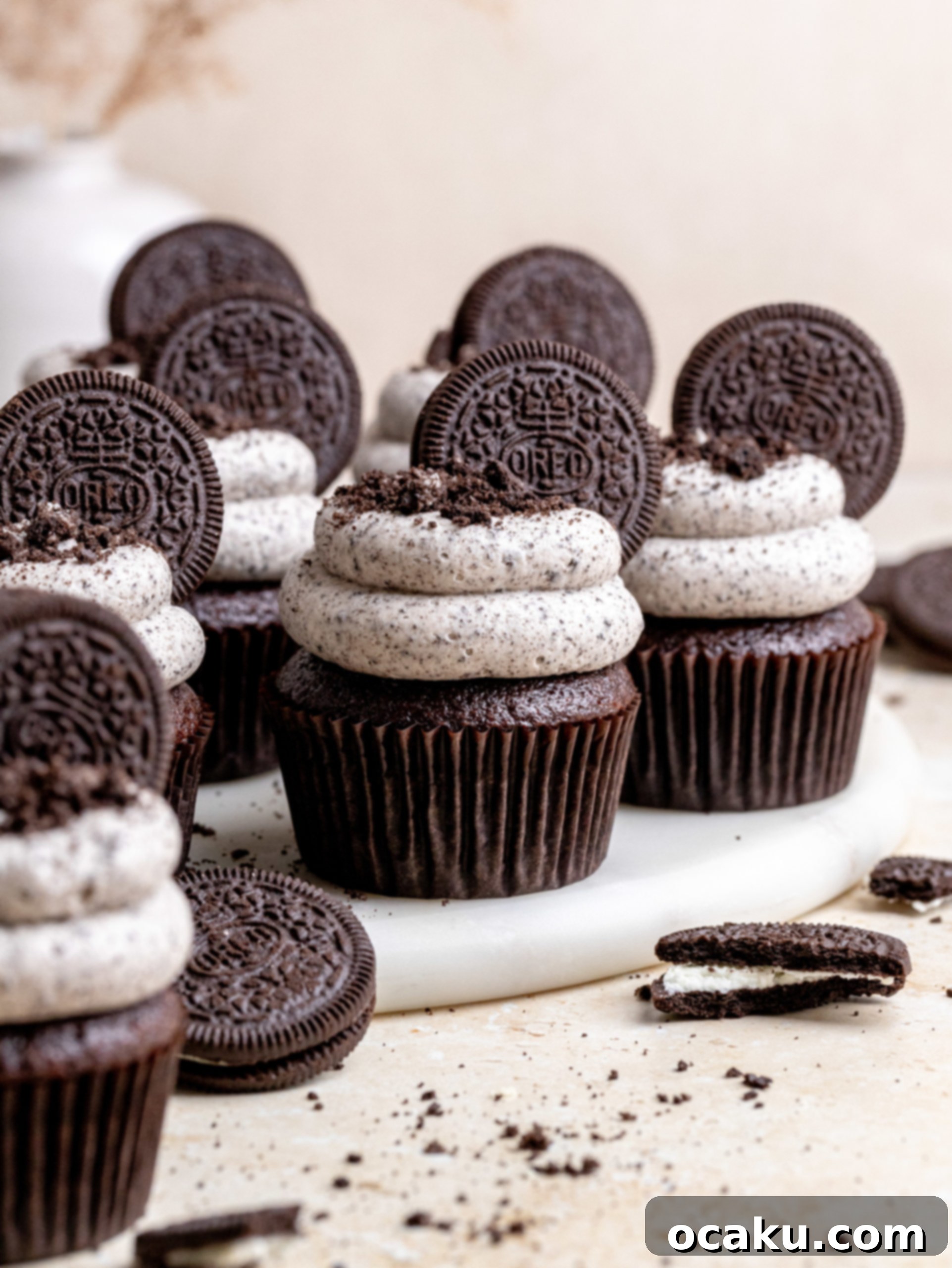 A hand piping Oreo buttercream onto a chocolate cupcake, illustrating the final decorating step.