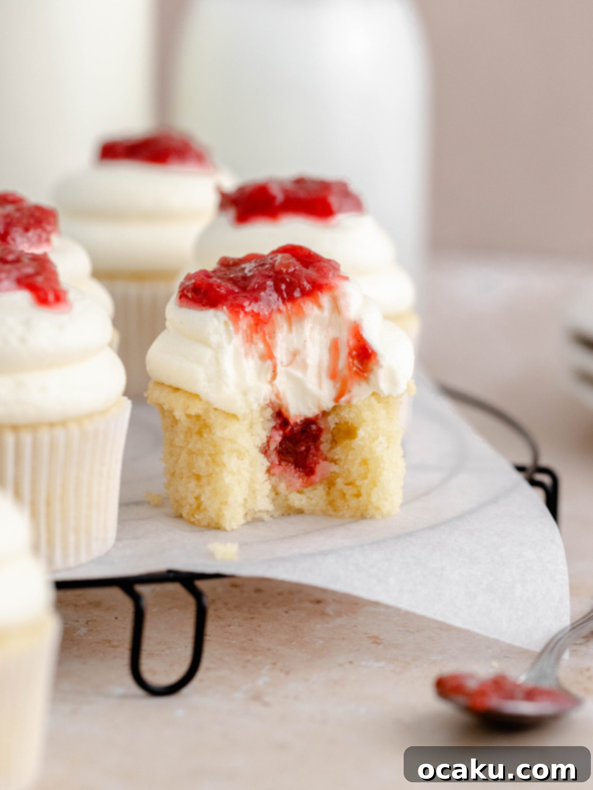 A perfectly baked rhubarb and almond cupcake with a bite taken out, revealing the pink rhubarb compote inside.