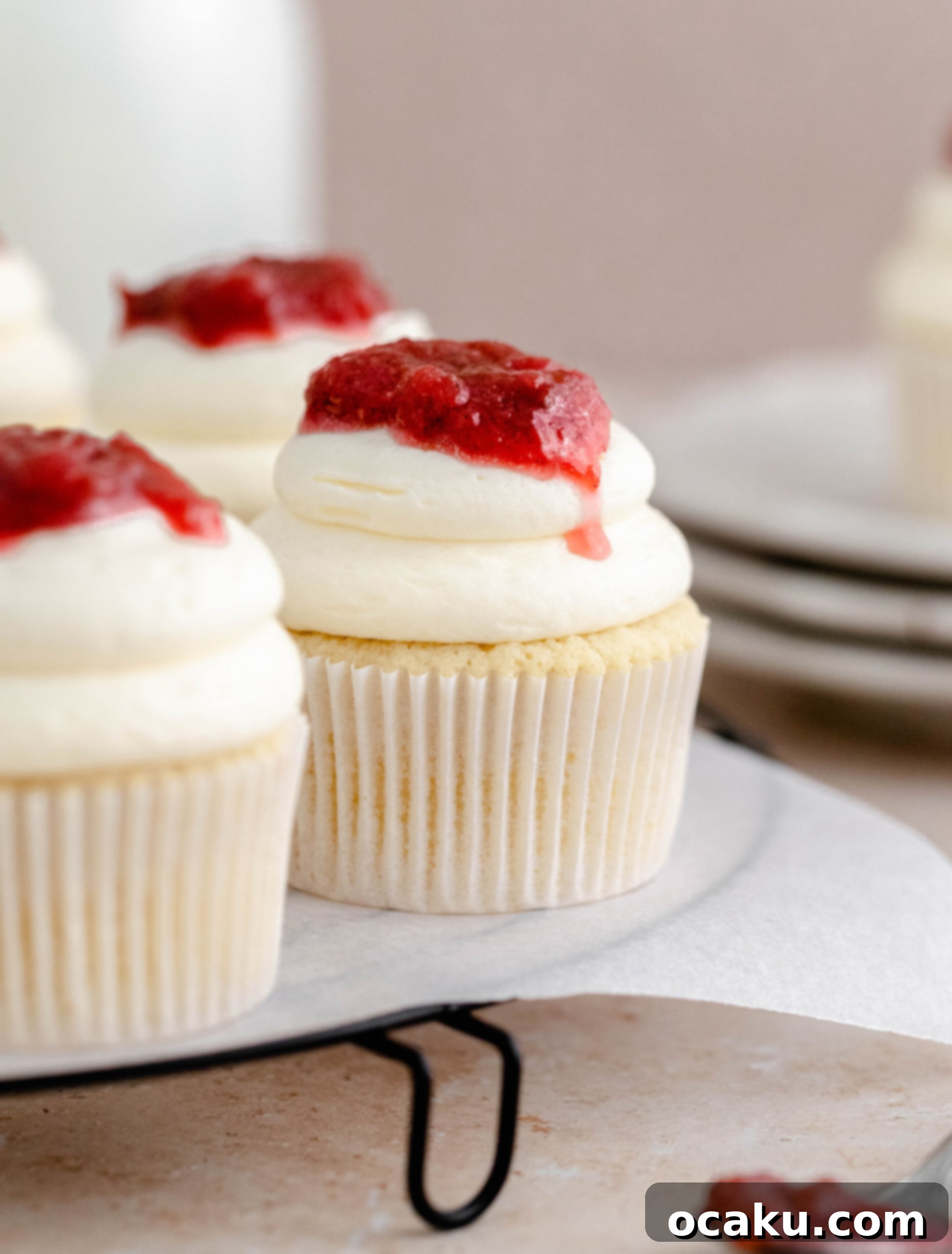 Three beautifully decorated rhubarb and almond cupcakes on a elegant cake stand.