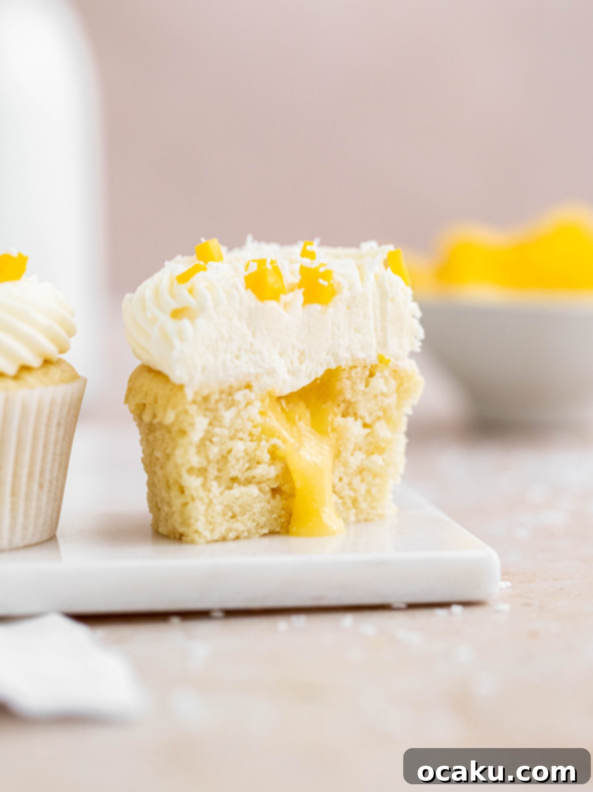 Mango Bliss Cupcakes 5 A coconut cupcake cut open, showcasing a vibrant mango curd filling gracefully spilling out, topped with a delicate coconut buttercream.