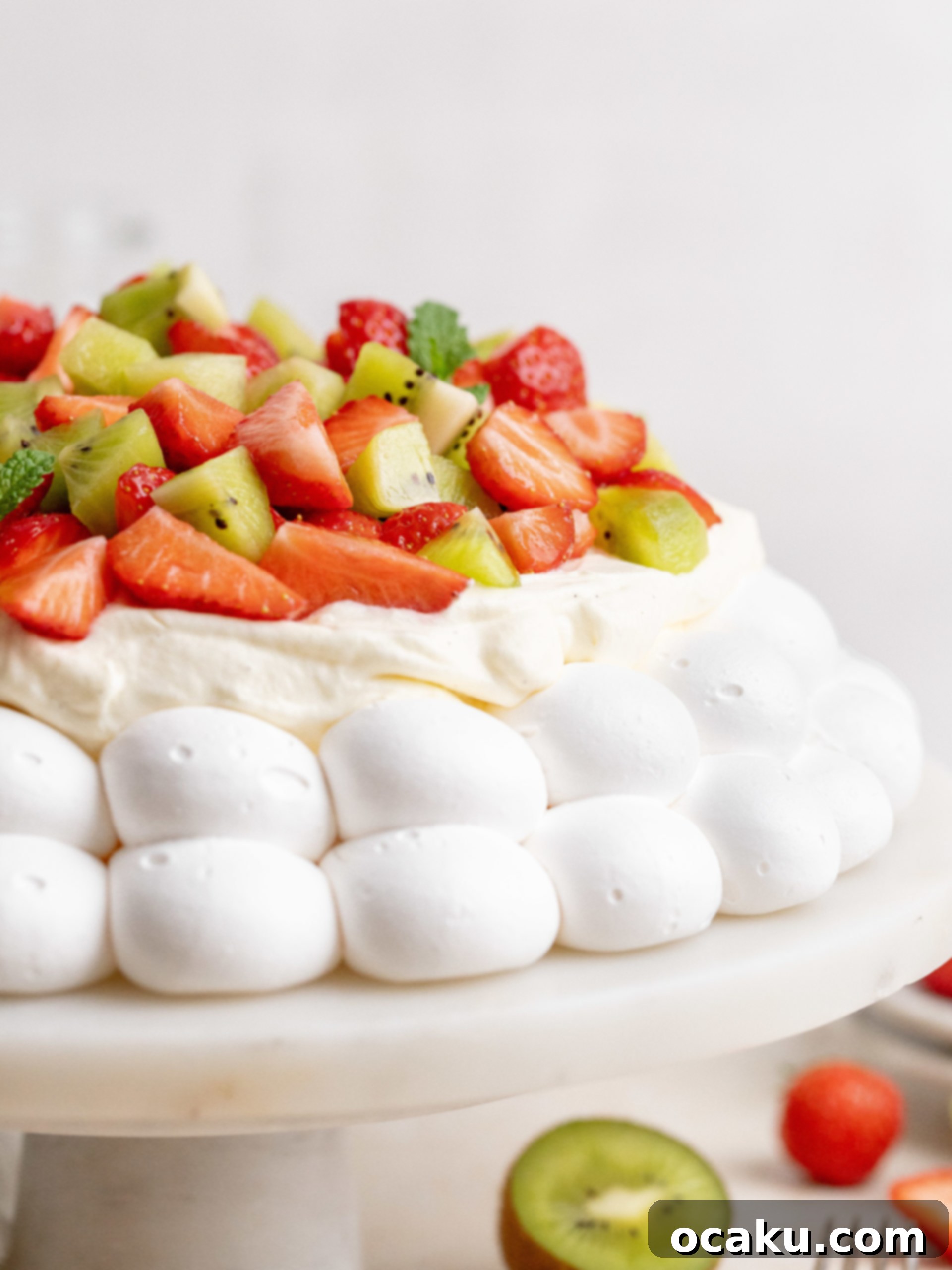 A beautifully decorated Summer Pavlova, garnished with fresh strawberries, kiwi slices, and green mint leaves on a white serving platter