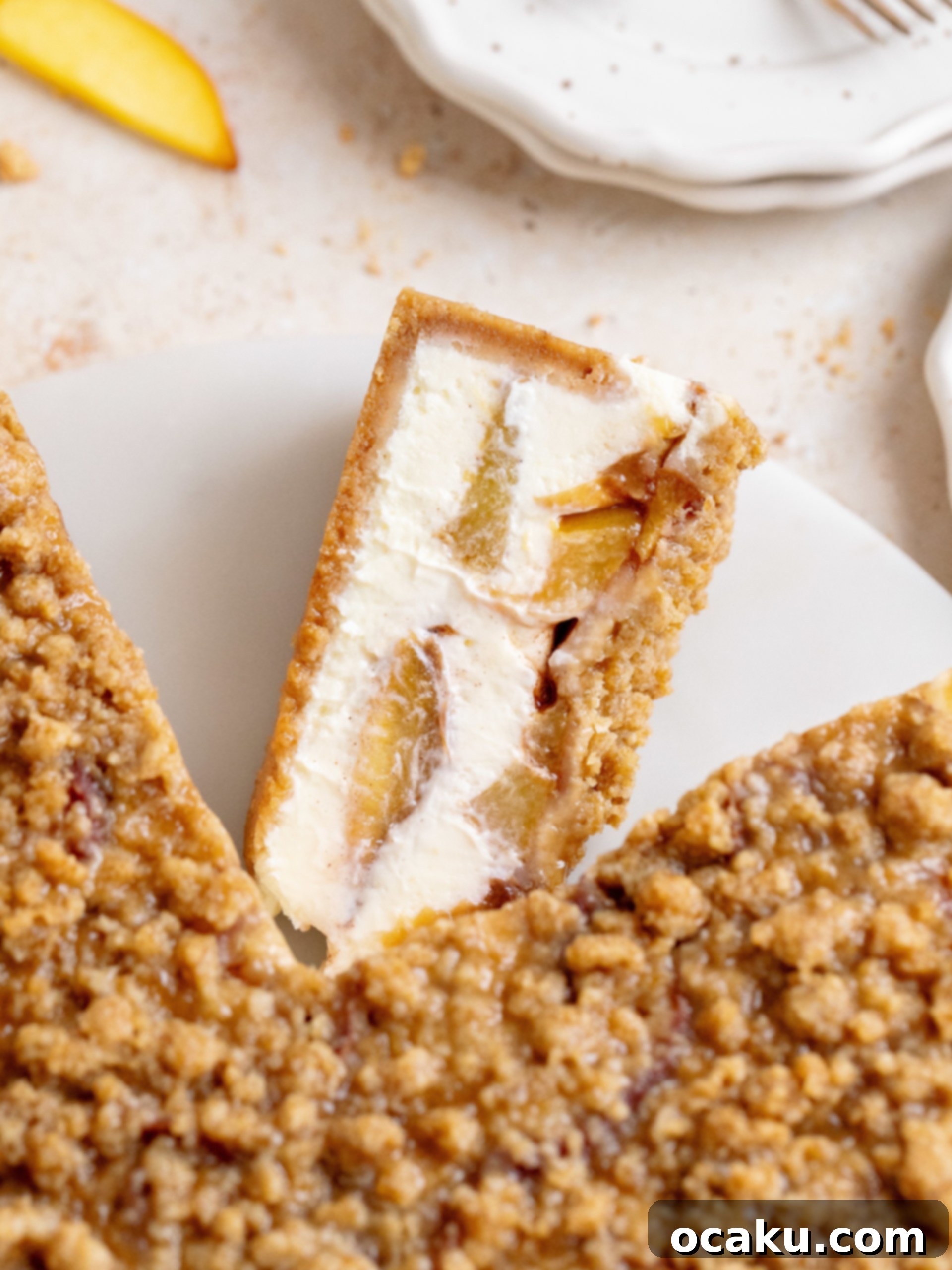 A slice of Peach Crumble Cheesecake with a dollop of whipped cream on top, showcasing the layers of crust, creamy cheesecake, baked peaches, and golden crumble.