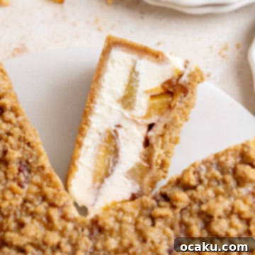 A whole Peach Crumble Cheesecake with slices missing, topped with crumble and fresh peaches.