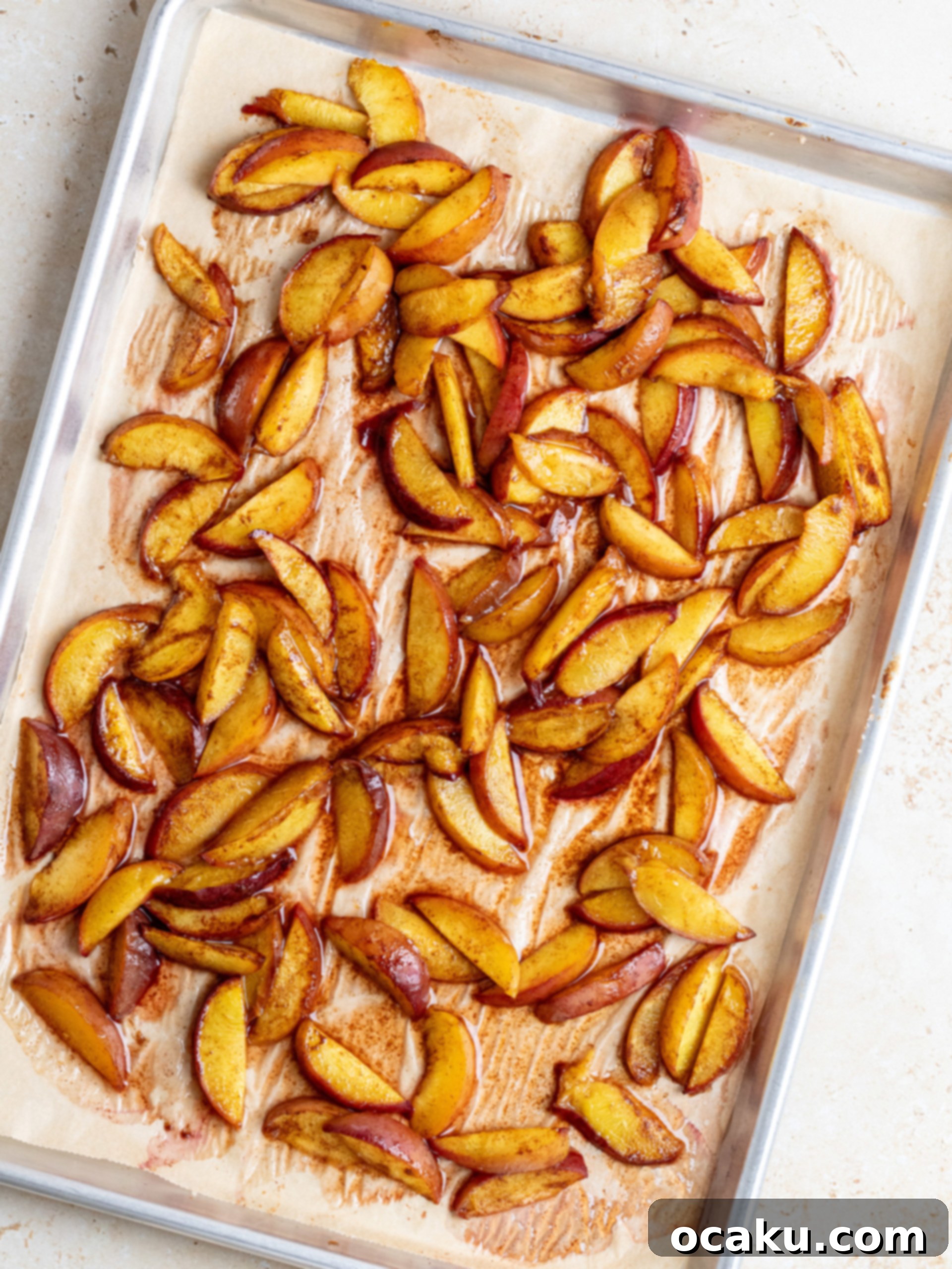 Sliced peaches tossed with sugar and cinnamon on a baking sheet.