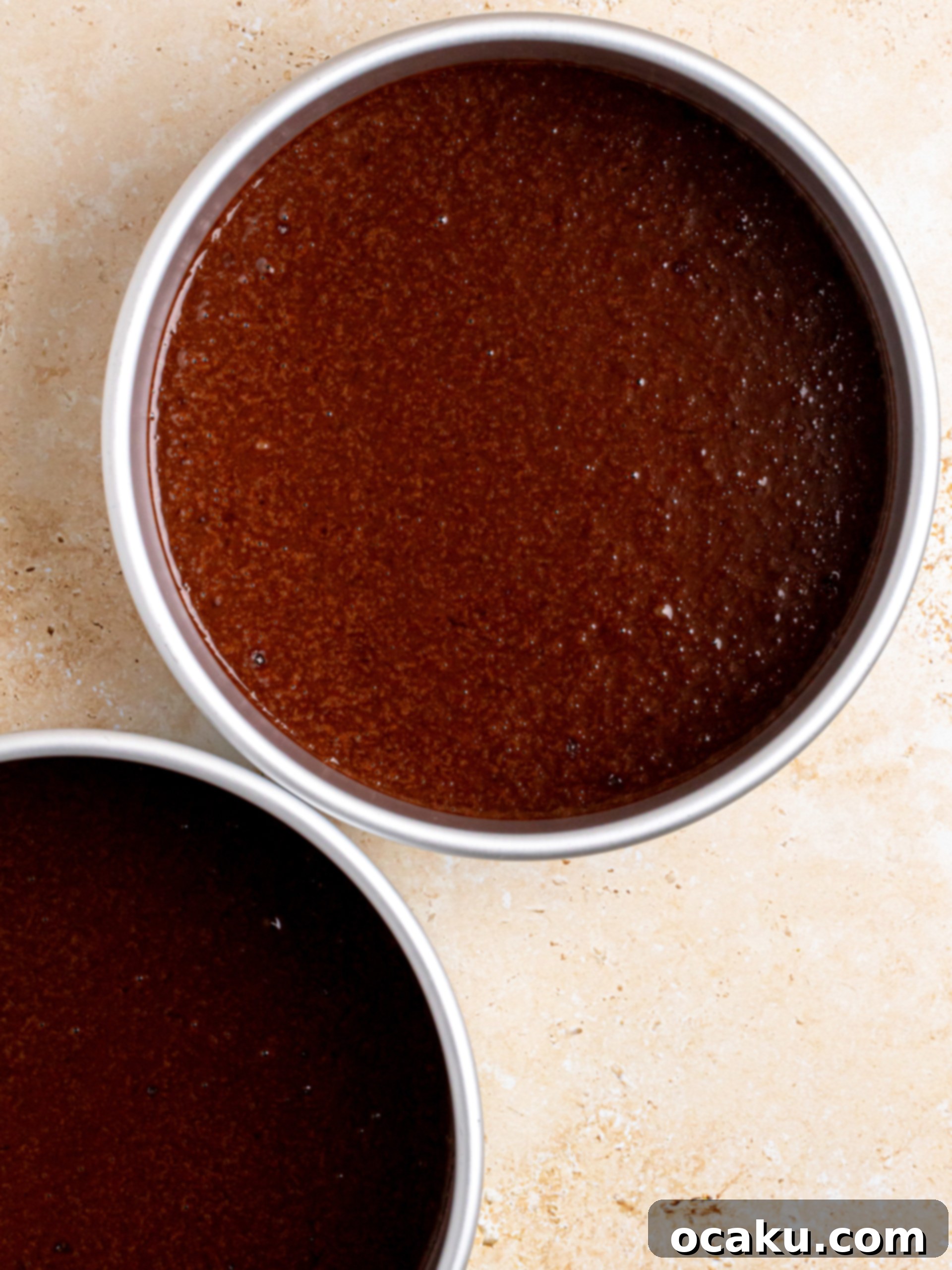 Chocolate cake batter being poured into lined baking pans.