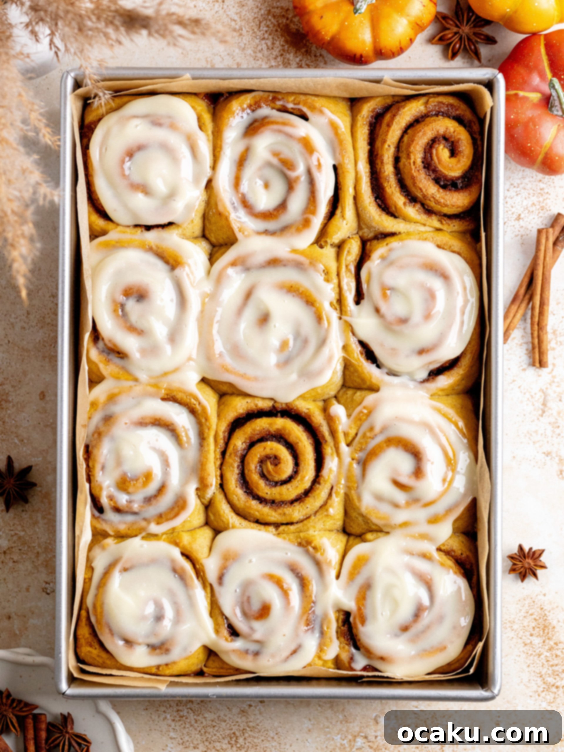 Freshly baked pumpkin cinnamon rolls in a baking dish, topped with maple cream cheese frosting.