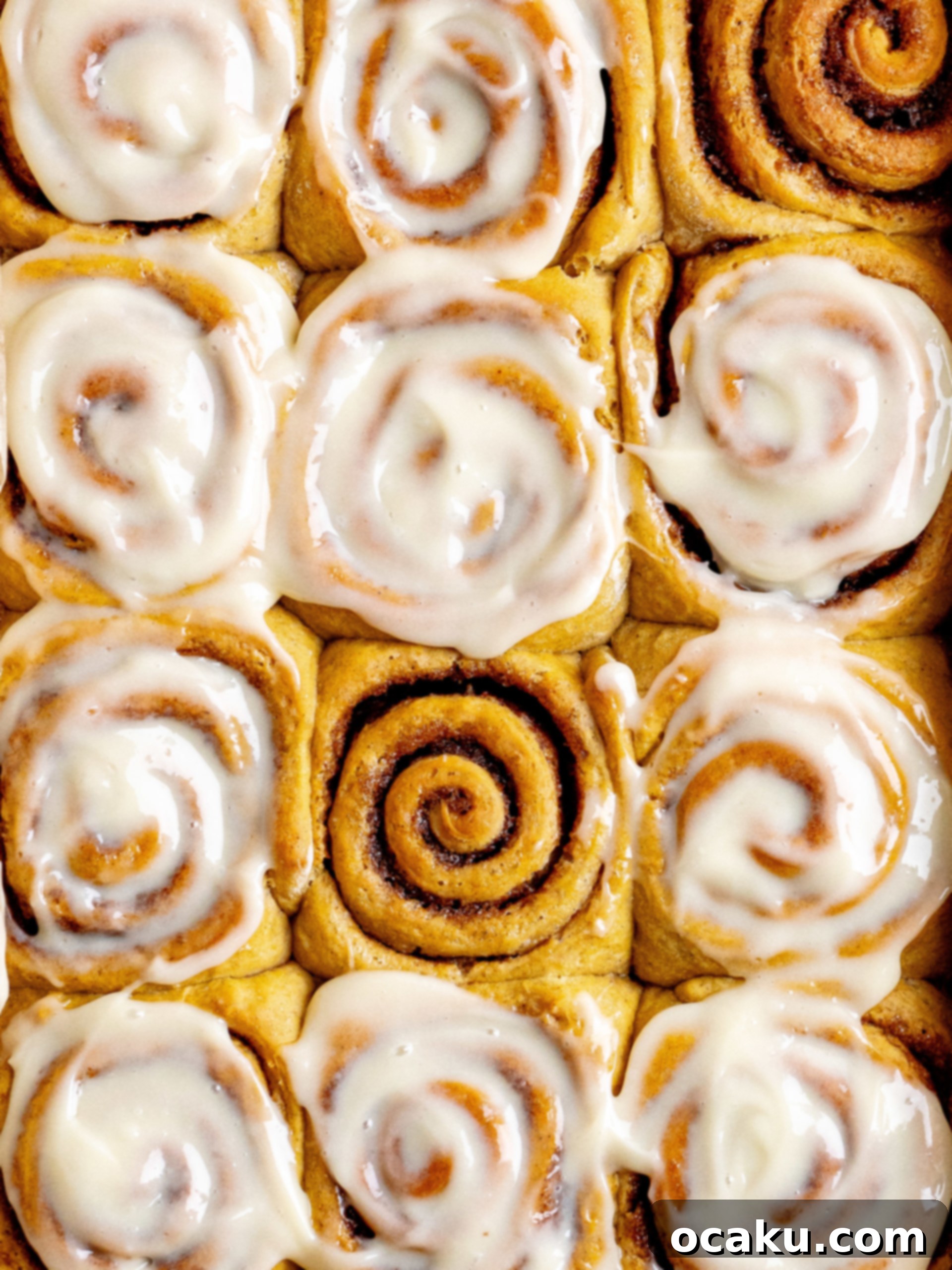 Several pumpkin cinnamon rolls in a baking dish, garnished with autumn leaves.