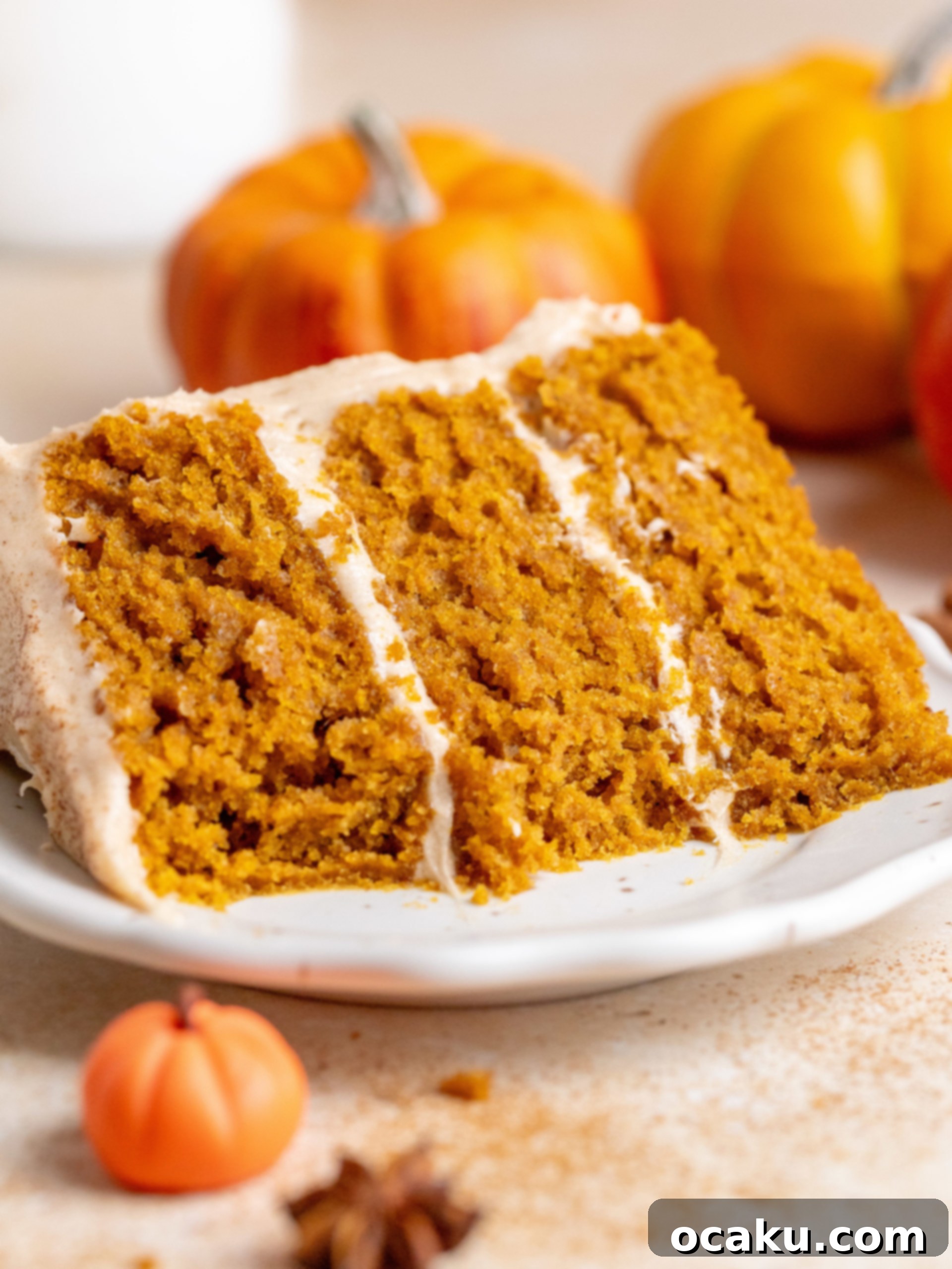 Close-up of a slice of pumpkin layer cake with cinnamon cream cheese frosting on a rustic wooden board