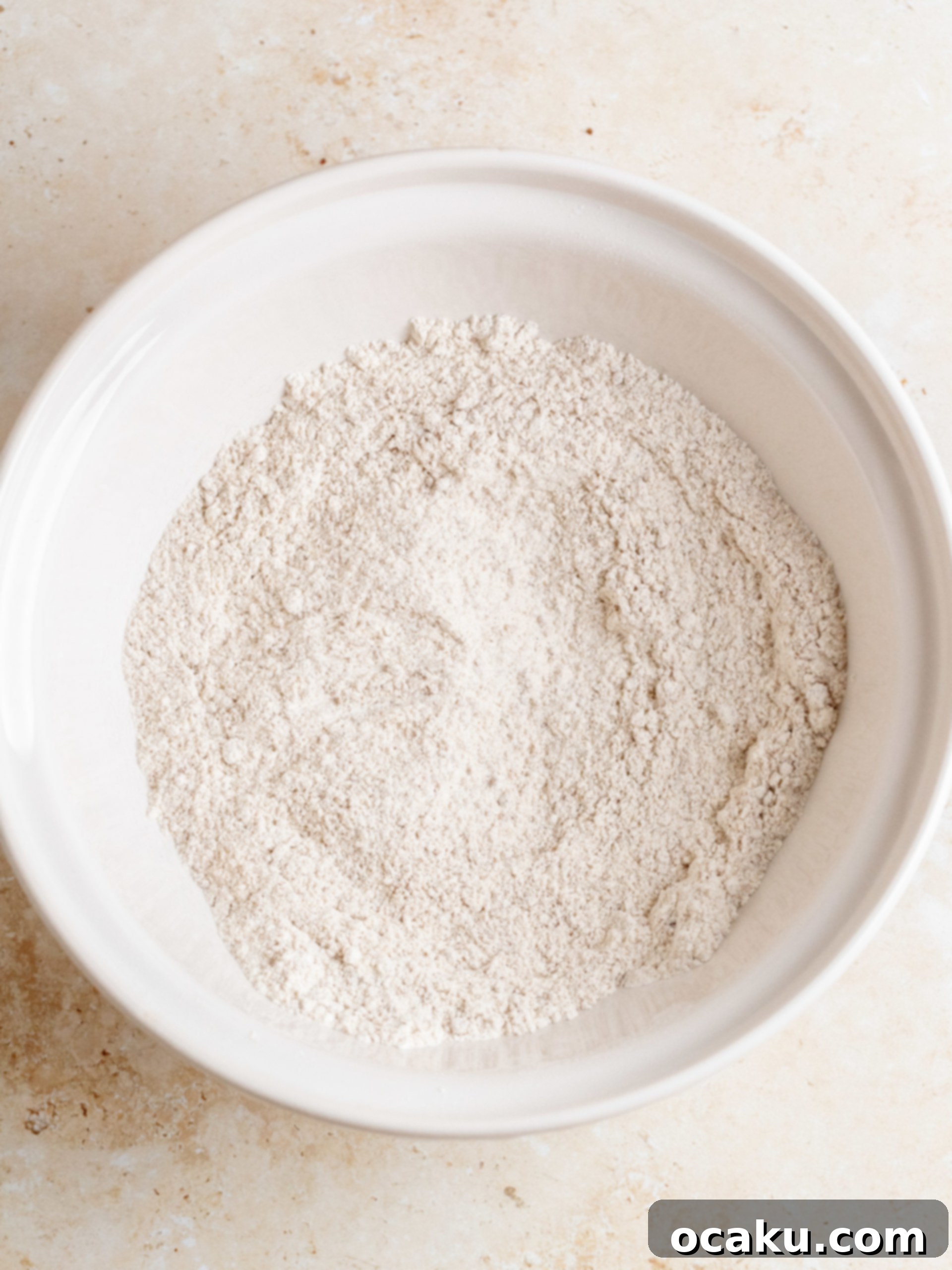 Gingerbread cake batter being poured into a prepared round baking pan, showing the rich, dark color.