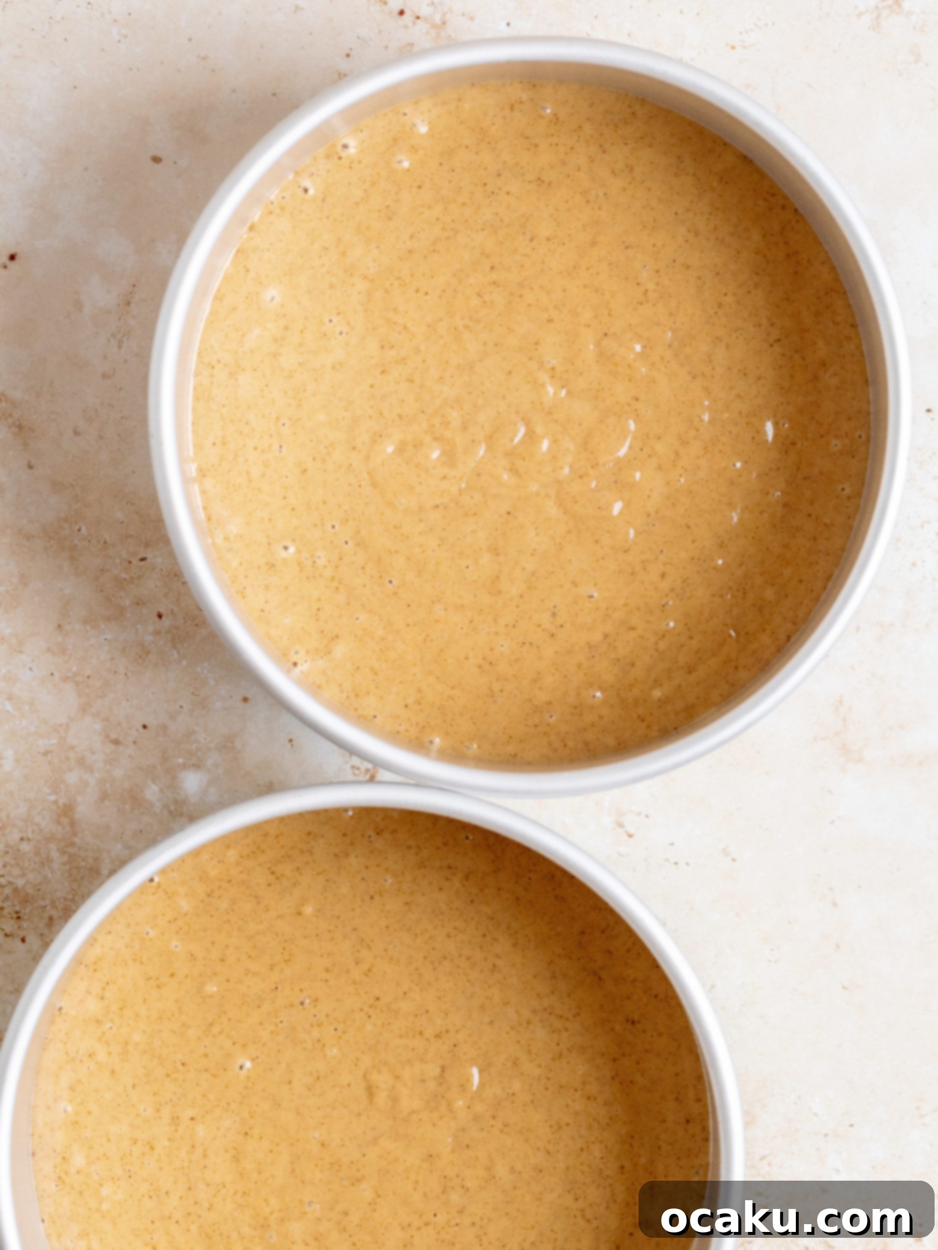 A baker applying the first layer of cream cheese frosting, the crumb coat, to a gingerbread cake.
