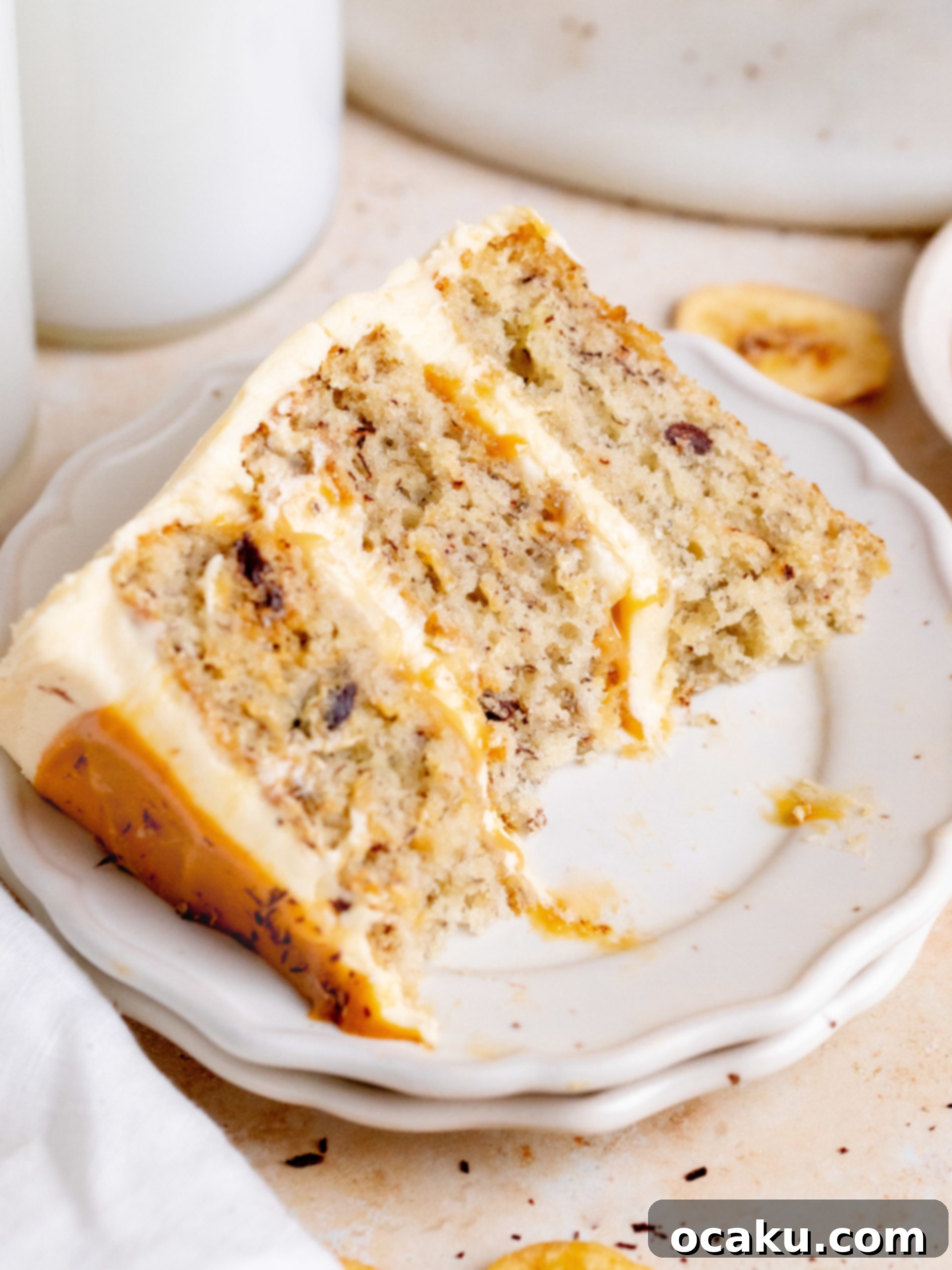 A high-angle shot of the completed Banoffee Layer Cake, highlighting its height, smooth frosting, and decorative dulce de leche drizzle, on a white cake stand.