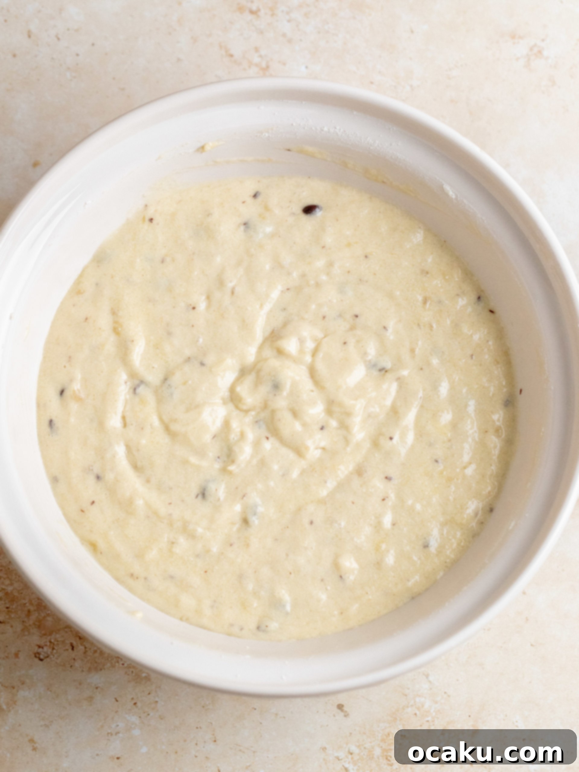 Banana cake batter being carefully divided into three perfectly lined round baking pans, ready for baking.