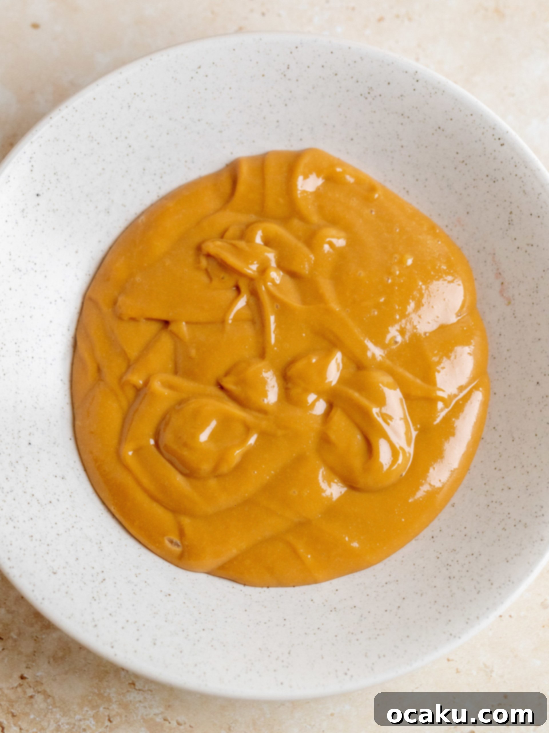 A cake layer being frosted generously with dulce de leche buttercream, with a distinct layer of fresh banana slices visible.