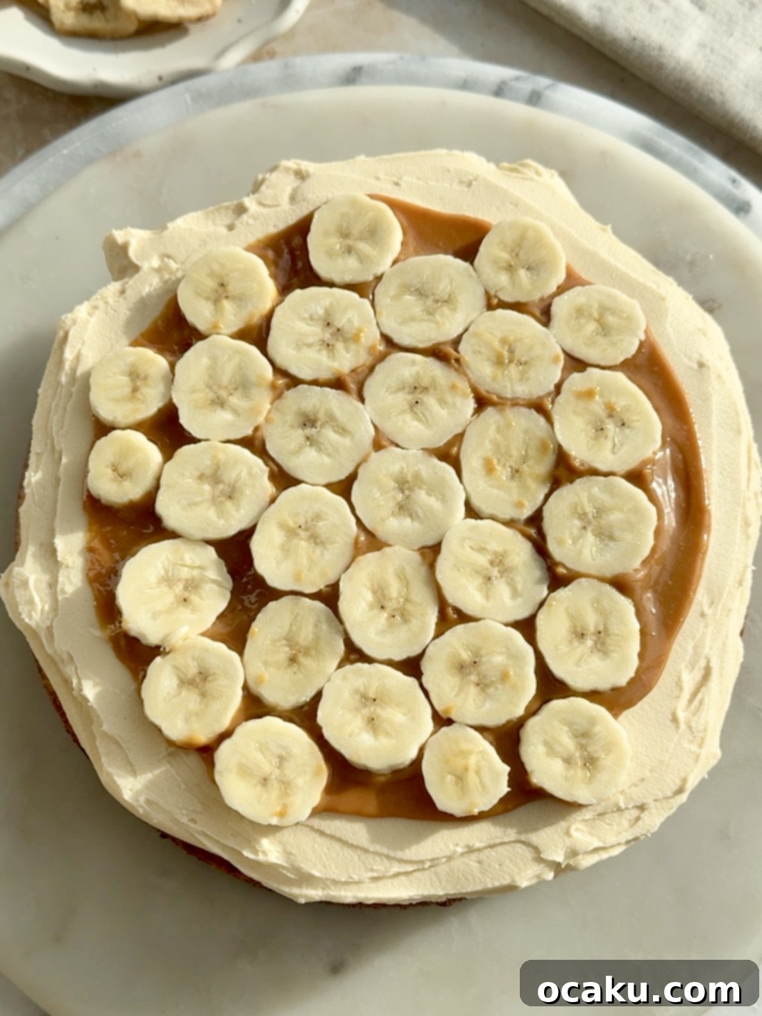 A beautifully decorated Banoffee Layer Cake, artfully drizzled with extra dulce de leche and adorned with chocolate shavings, resting on a cake stand.