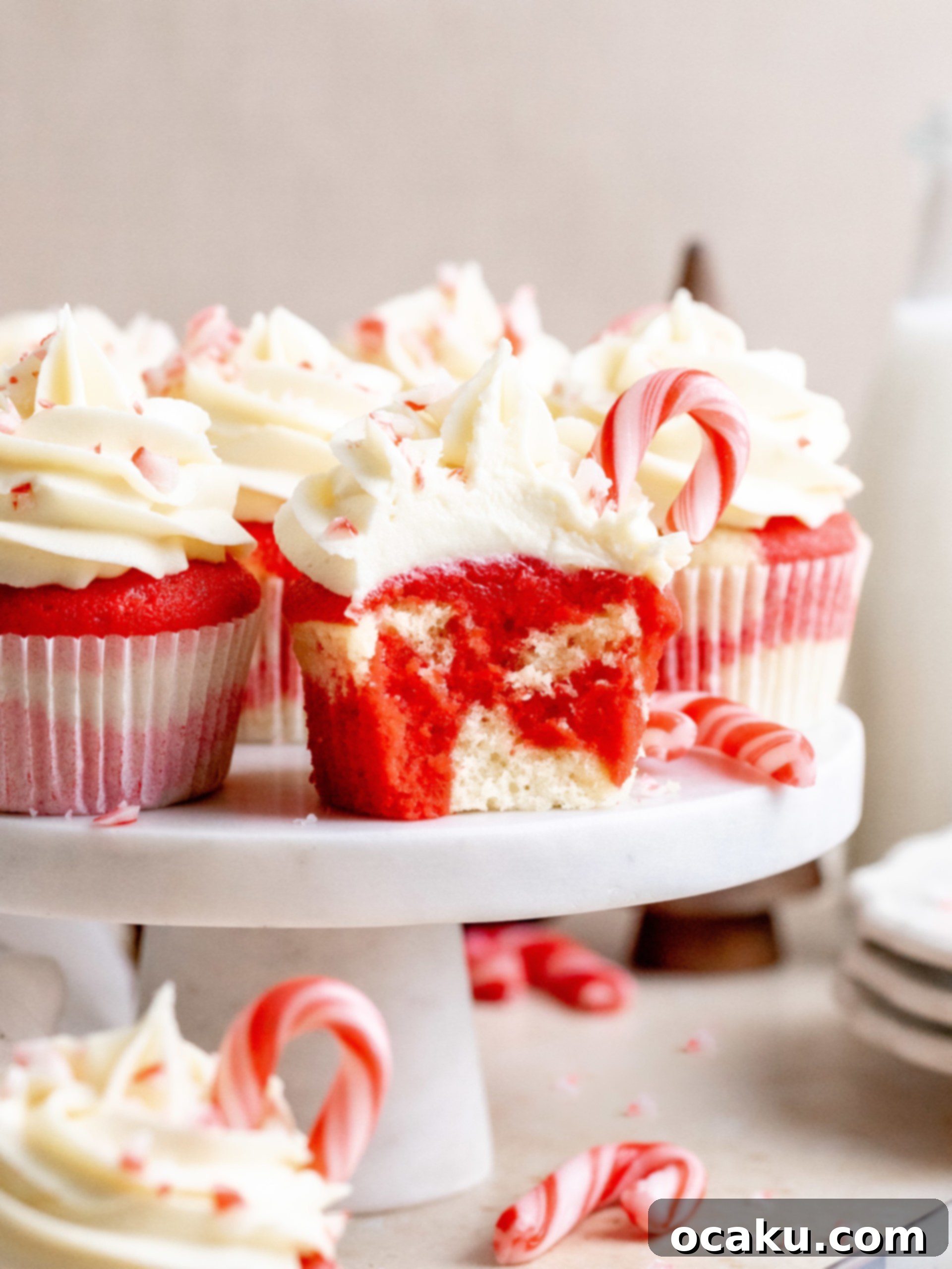 Two white chocolate peppermint cupcakes on a wooden board with candy canes.