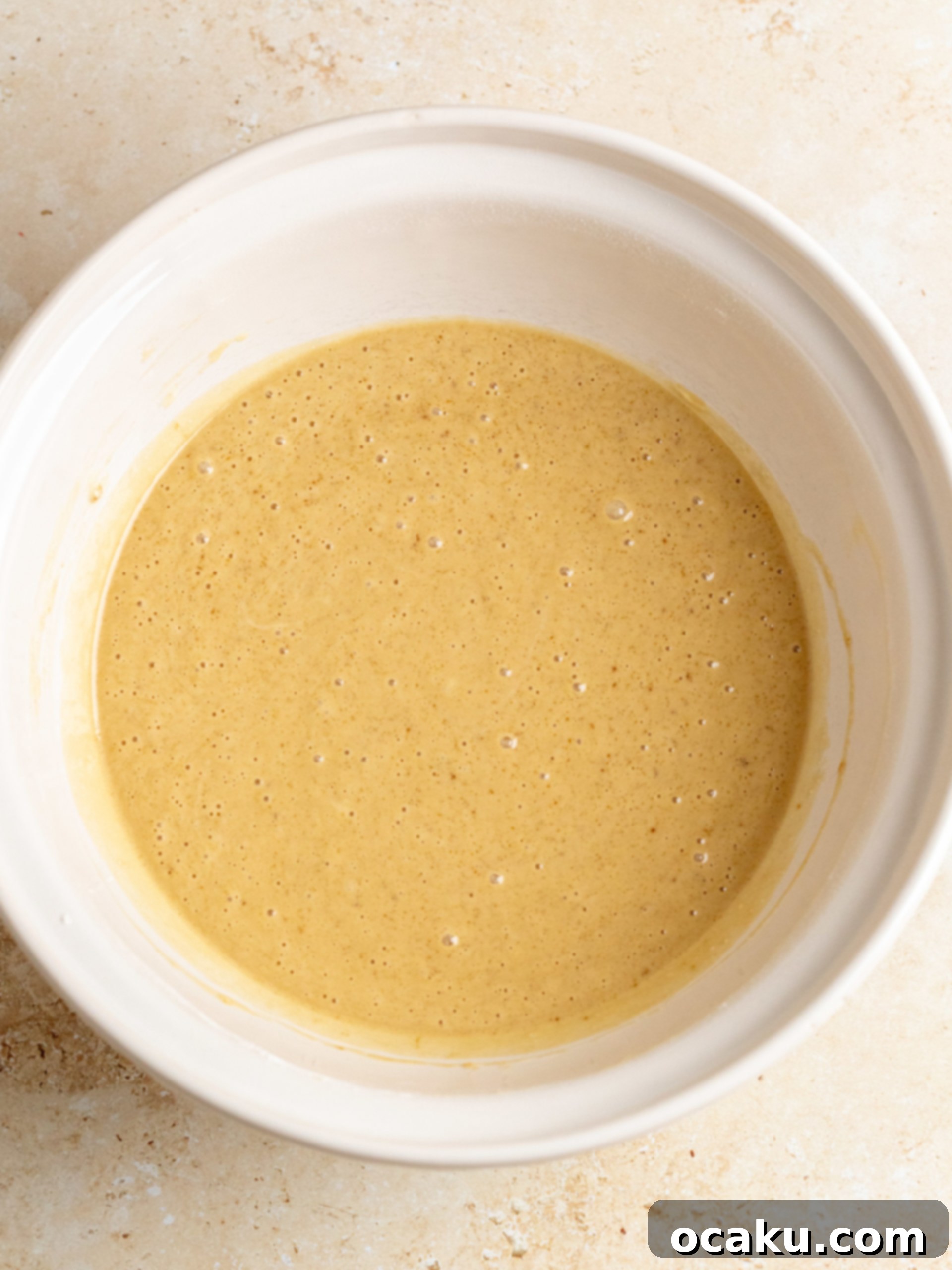 Step-by-step image showing Biscoff spread being added to creamed butter in a stand mixer.