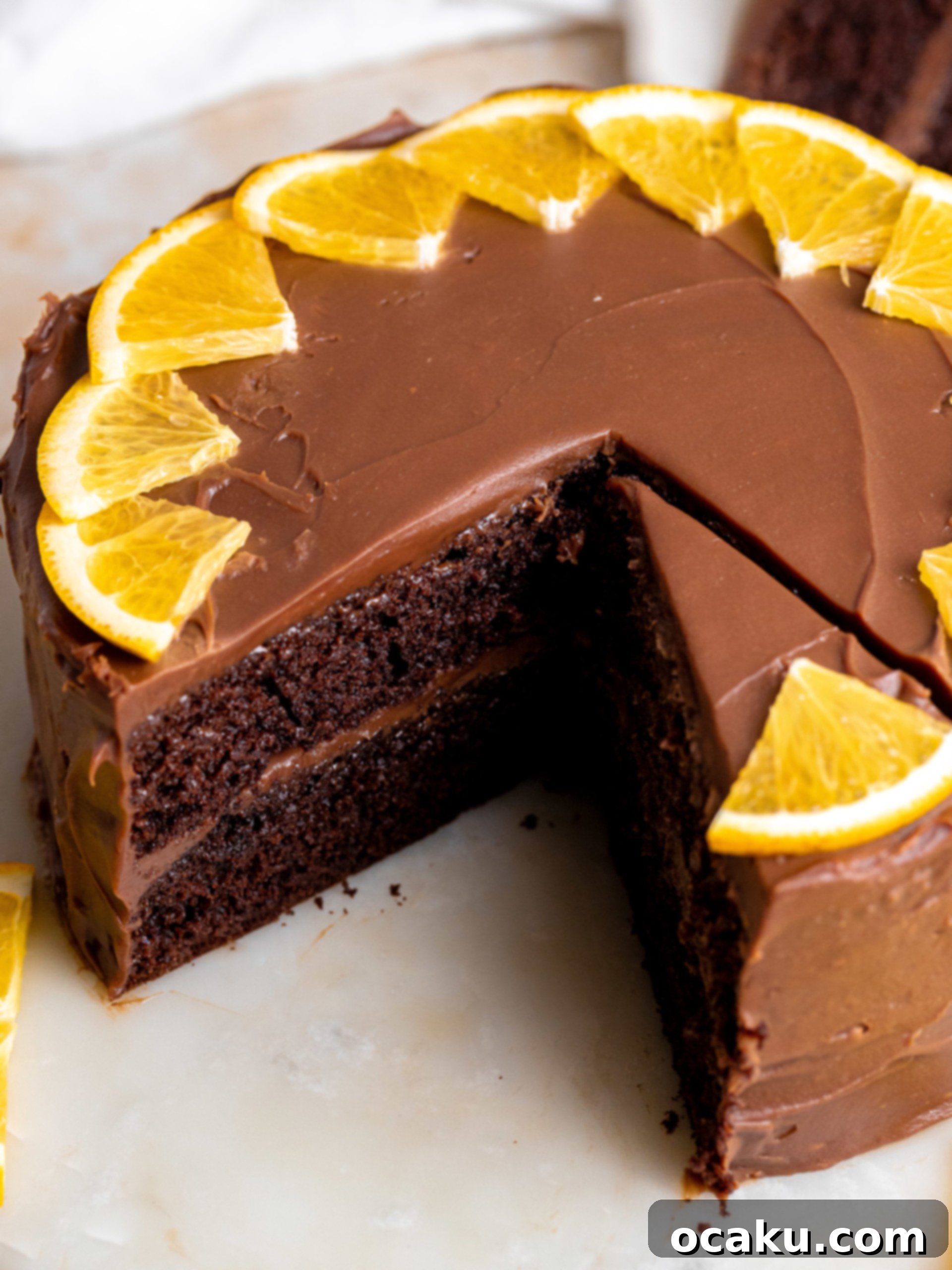 A beautifully decorated chocolate orange layer cake with fresh orange slices on top, showcasing its moist texture and rich ganache.
