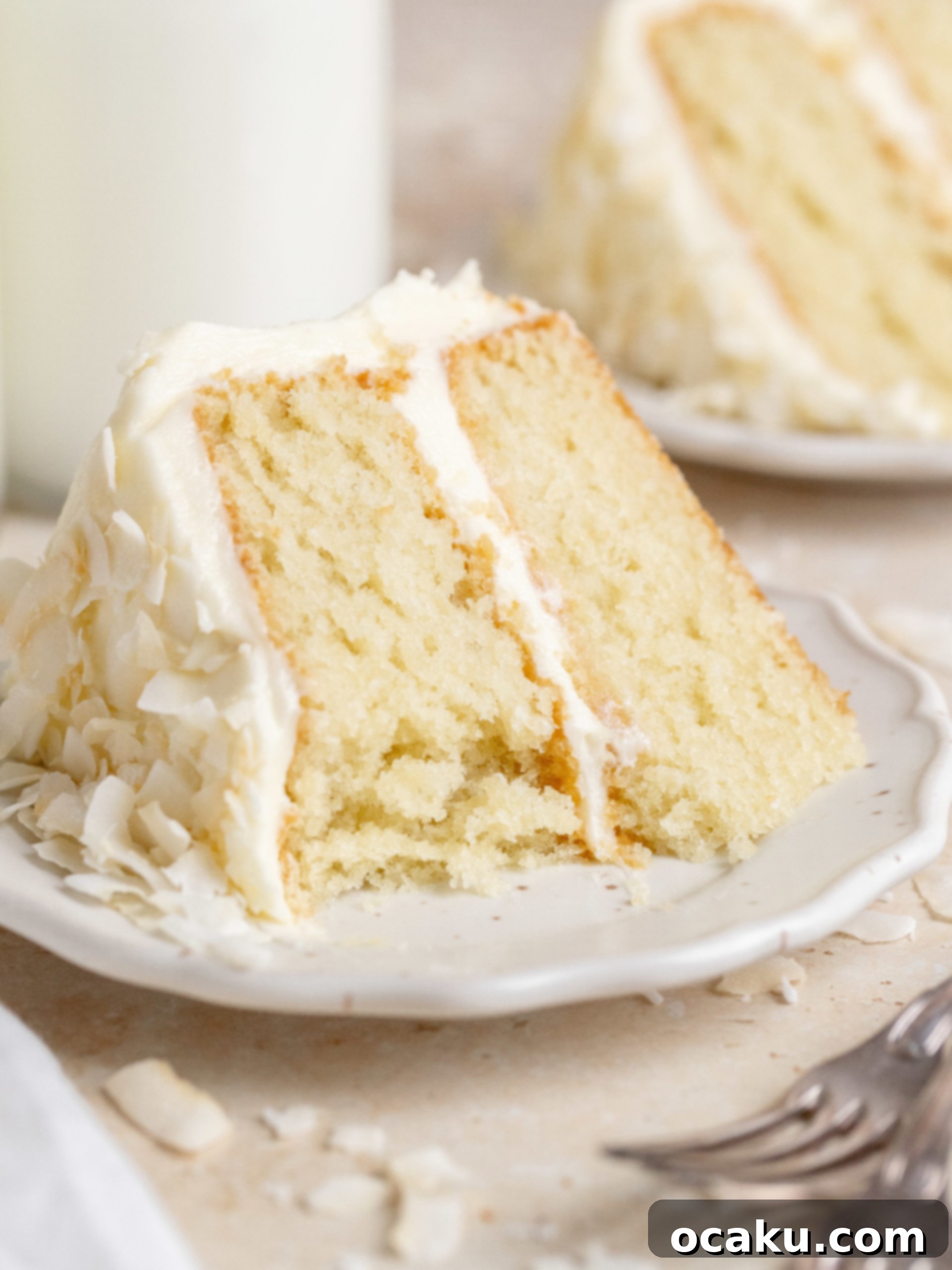 Ultimate Coconut Cloud Cake 9 A slice of coconut cake on a plate next to the whole cake