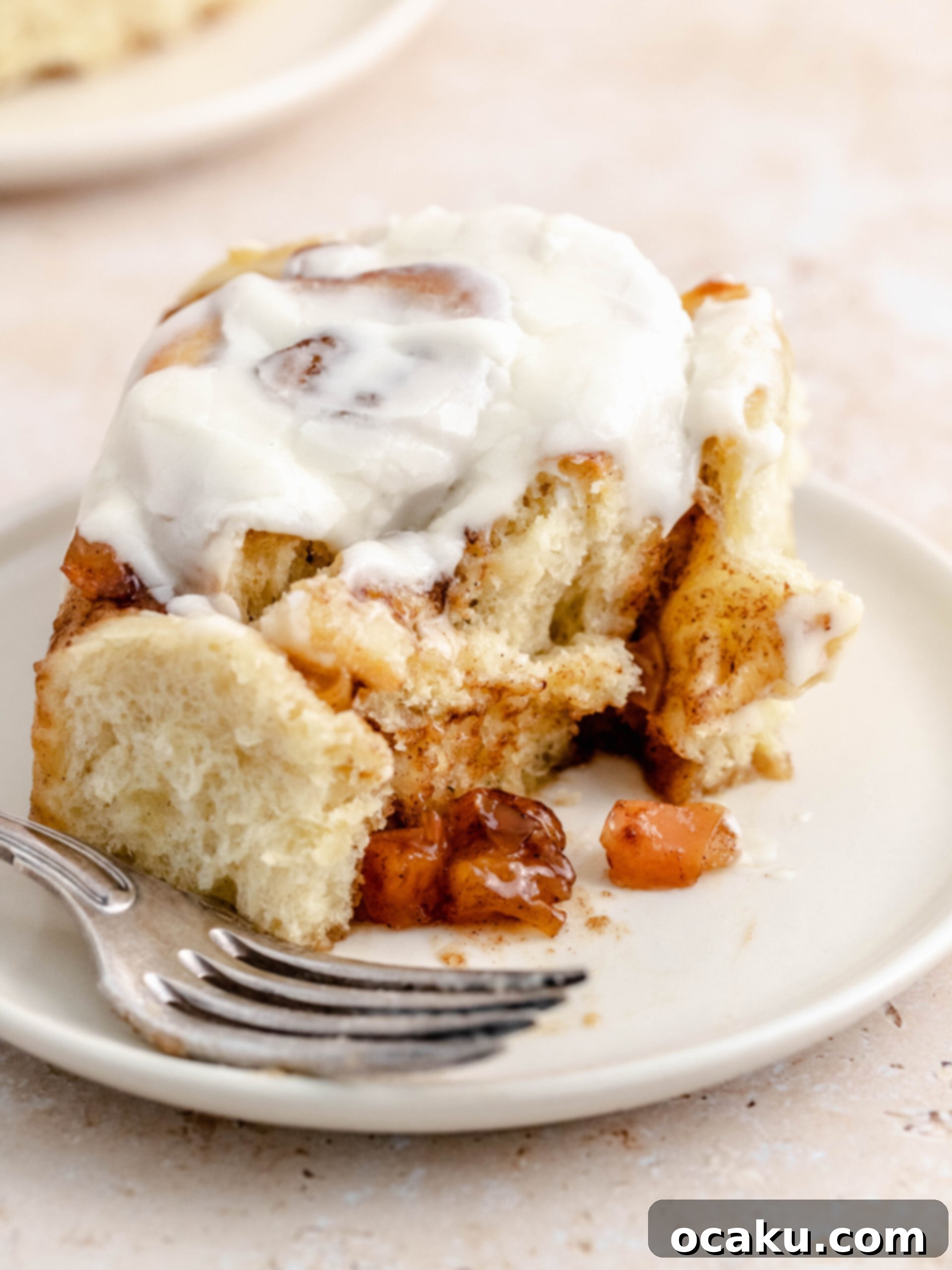 A close-up of a single apple pie cinnamon roll with a bite taken out, showing the gooey filling and soft dough.