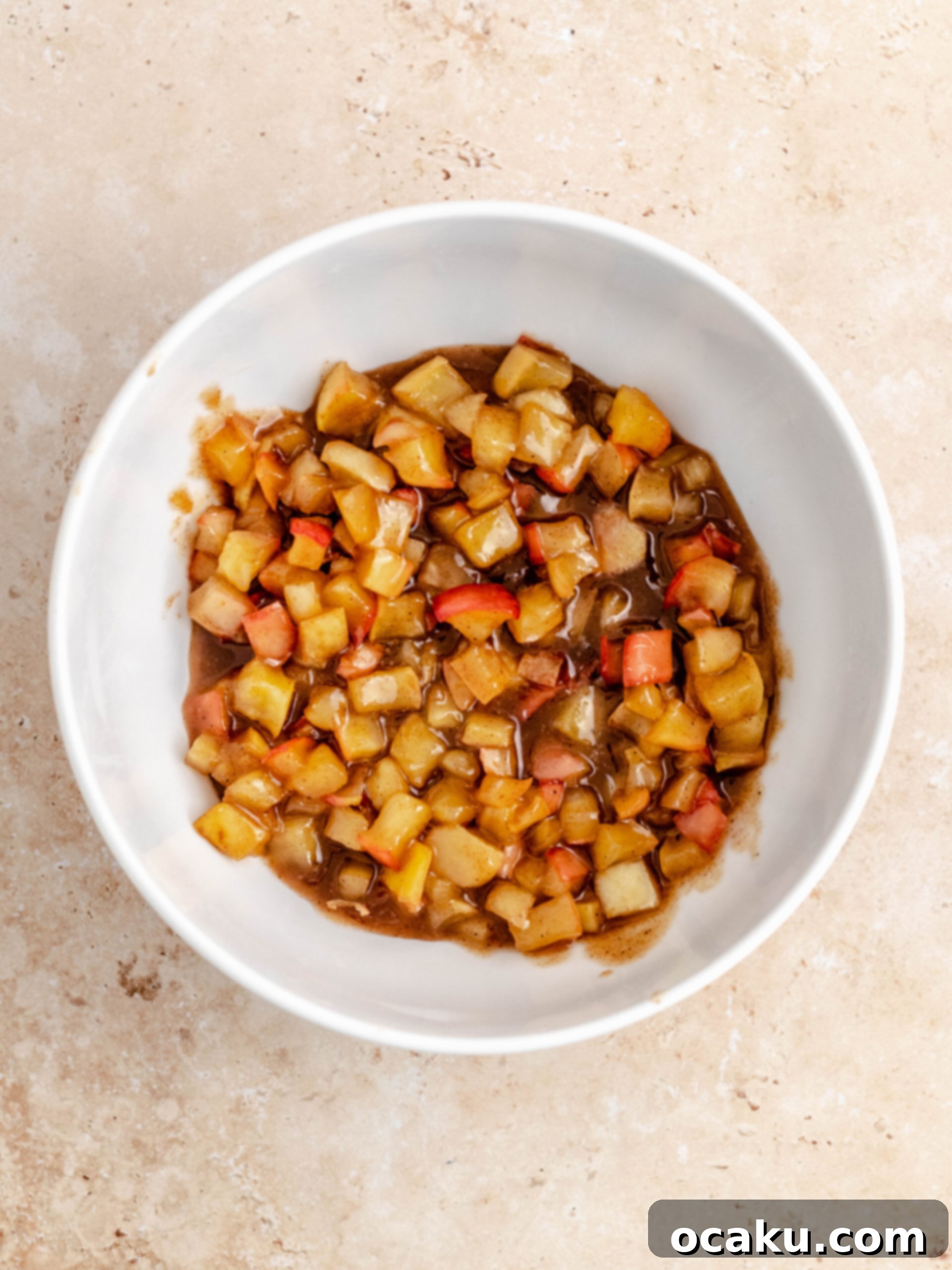 Close-up of freshly made apple pie filling in a glass bowl, featuring tender apple chunks and spices.