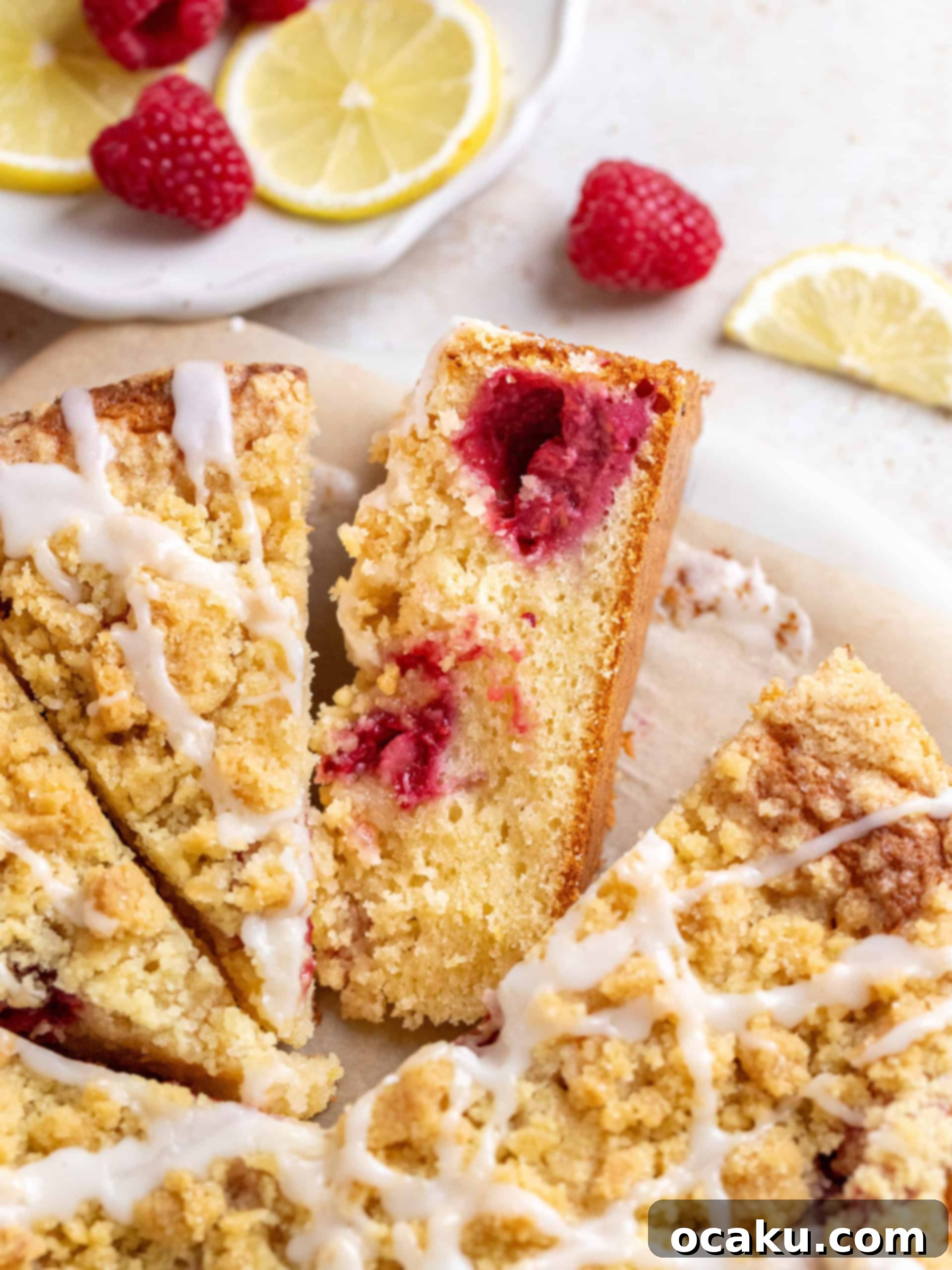 Zesty Raspberry Coffee Cake 2 A slice of moist raspberry lemon coffee cake with streusel topping and lemon glaze on a plate, with whole cake in background.