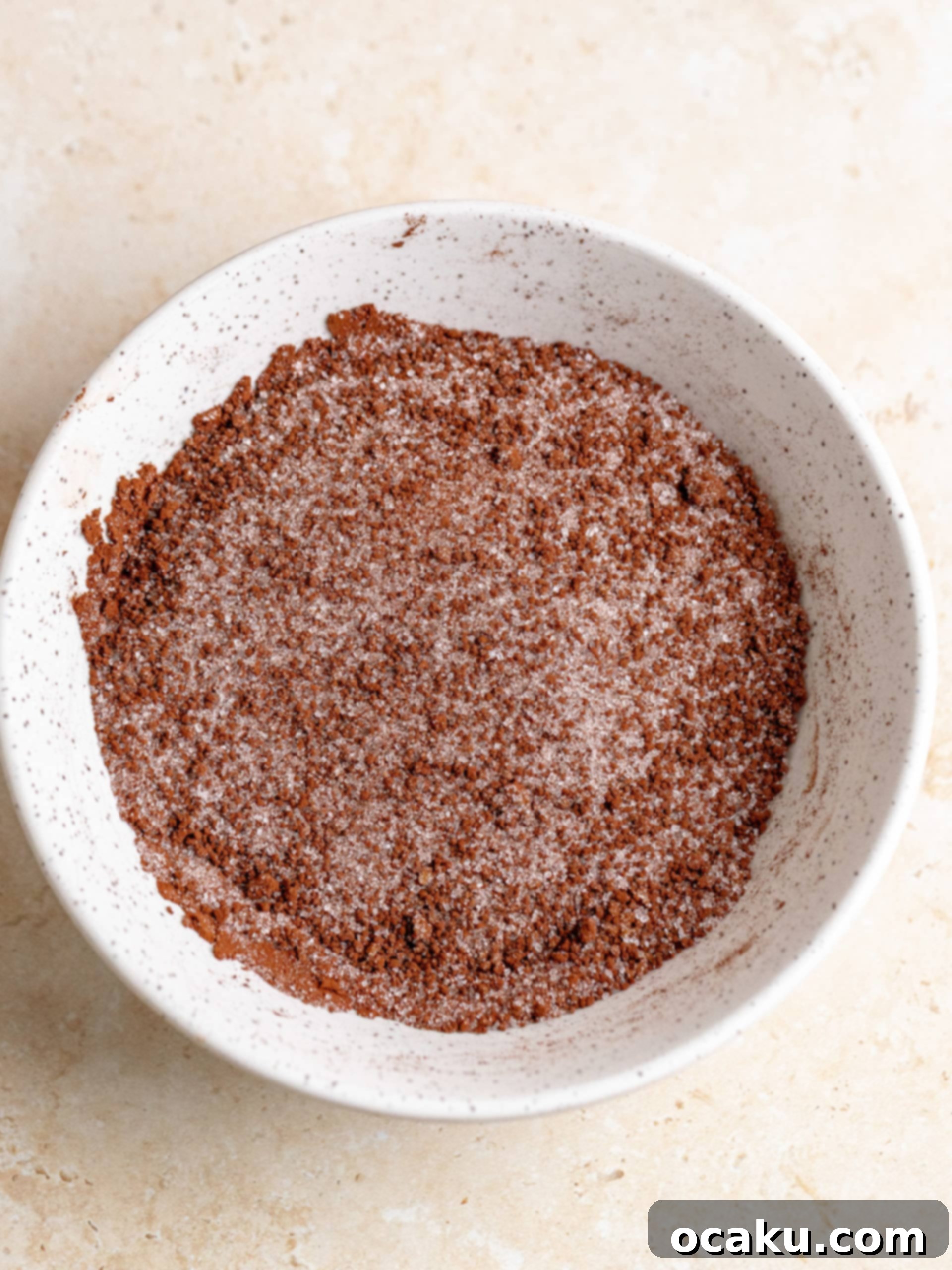Boiling water being carefully poured over the dry fudge mixture using the back of a spoon to ensure even distribution.