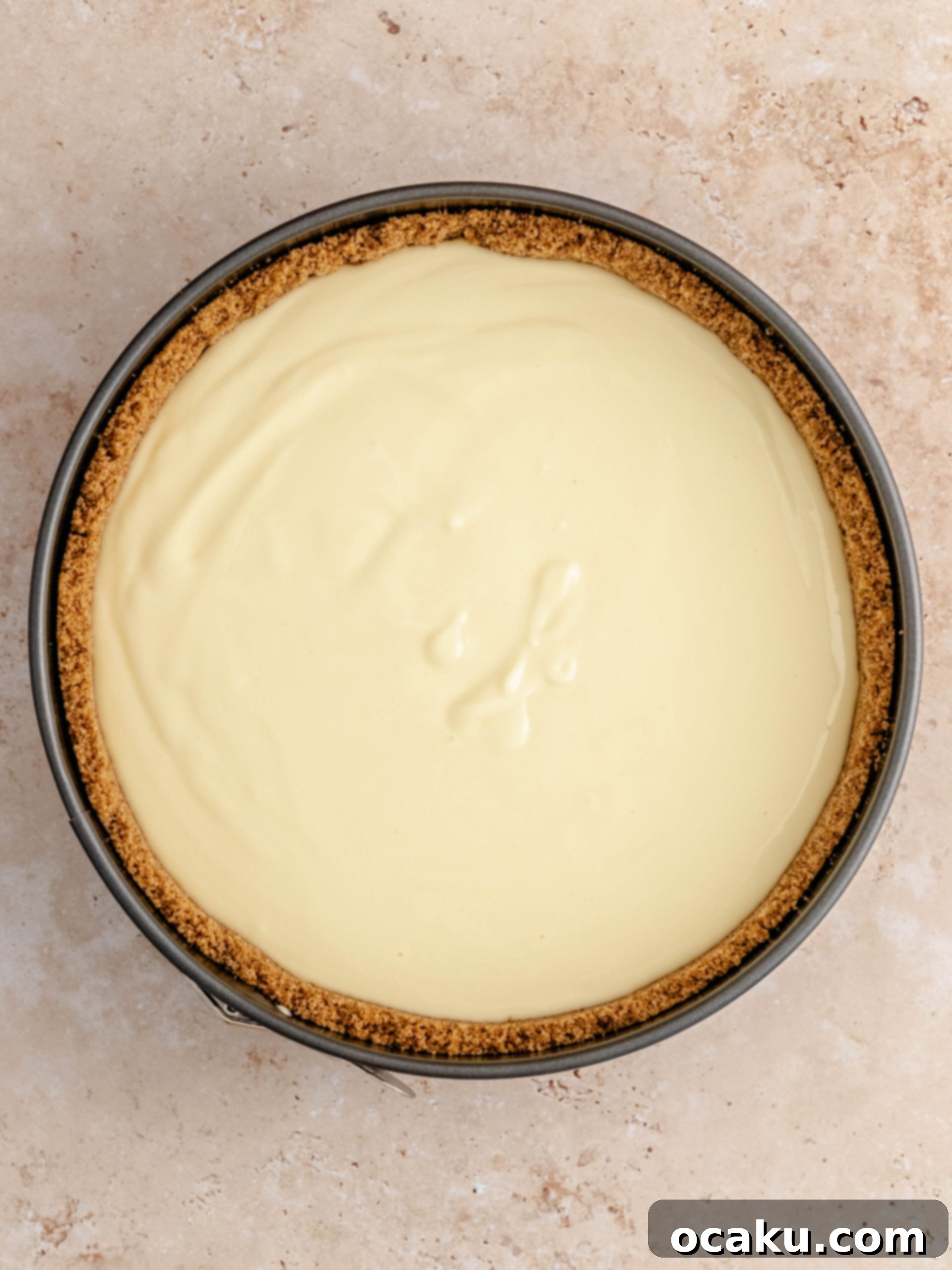 Rich cheesecake filling being poured evenly over the spiced cookie crust in a springform pan.