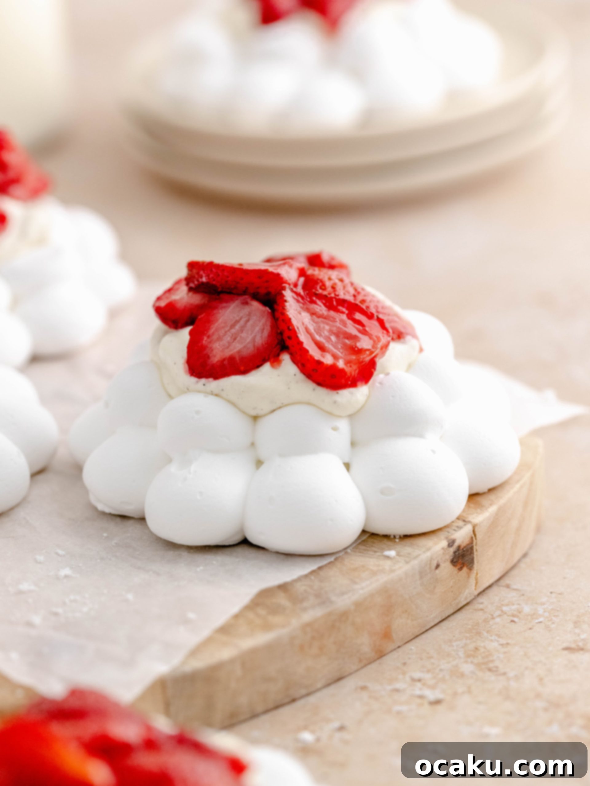 Baked strawberry meringue nest on cake tray. Golden-brown meringue, white cream, and bright red strawberries. The dessert is presented on an elegant cake stand with other nests in the background.