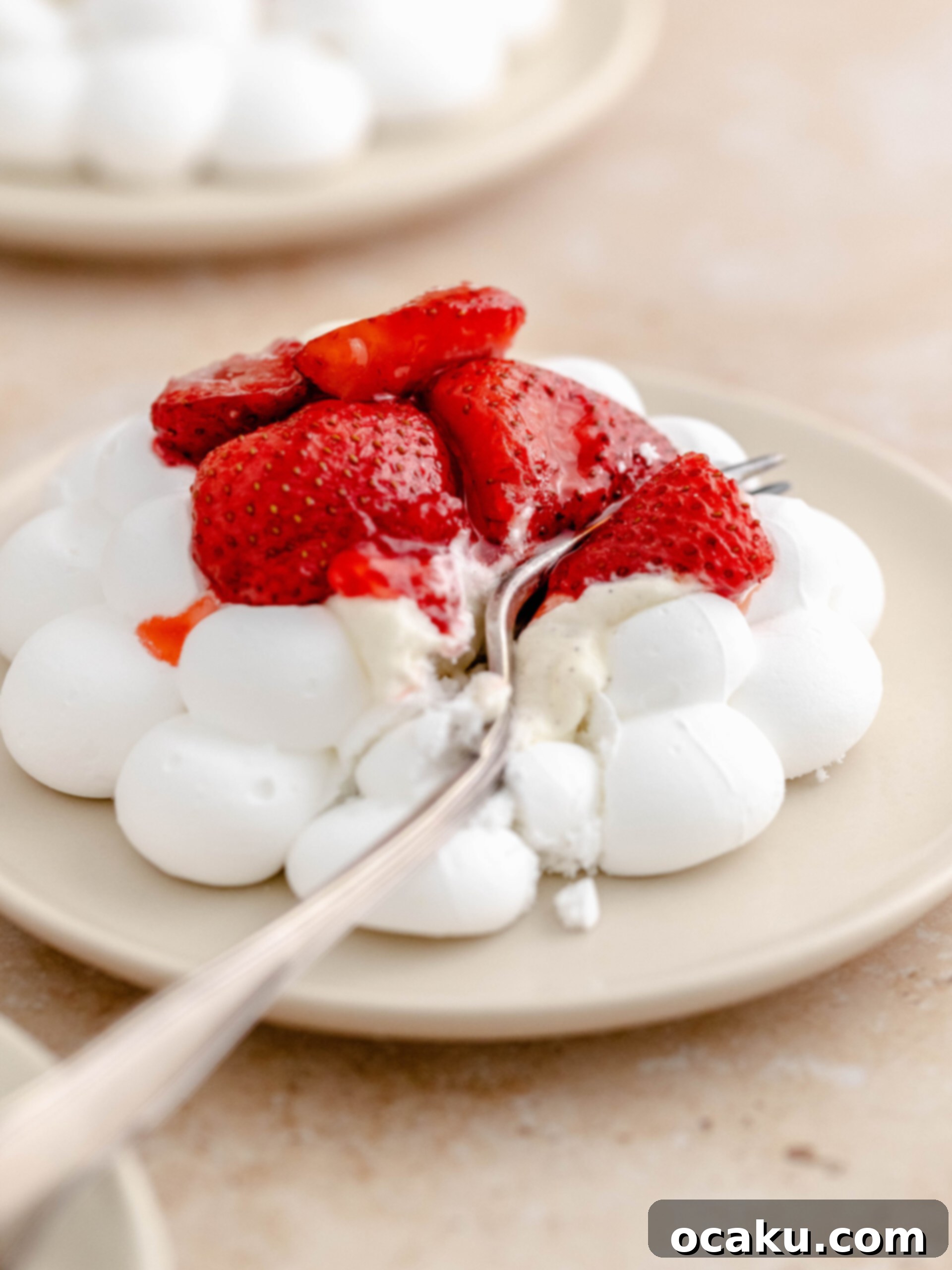 A baked strawberry meringue nest on a plate. The meringue is perfectly crisp, filled with white Chantilly cream, and topped with rich red baked strawberries.