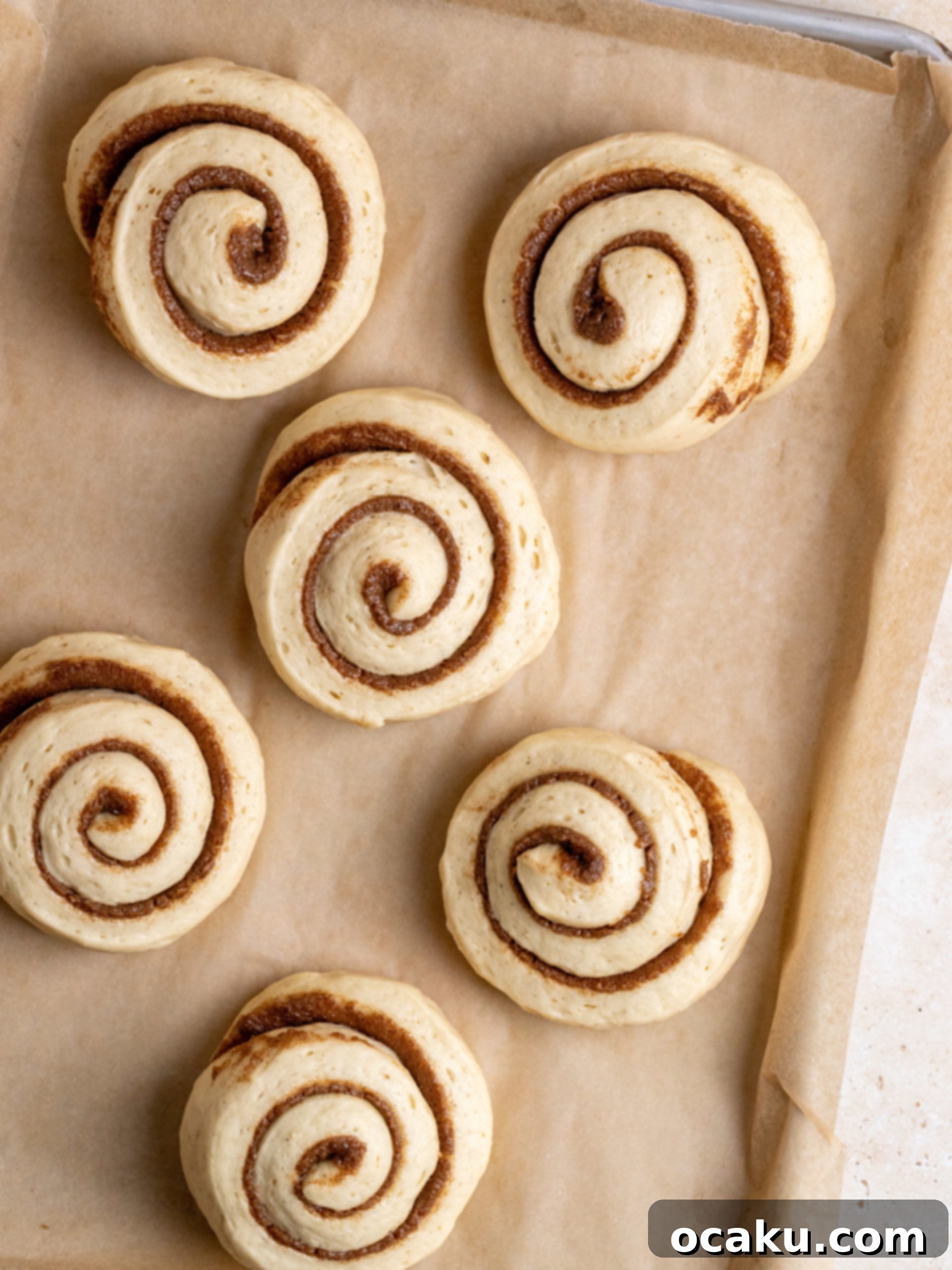 An overhead shot of two giant frosted cinnamon rolls on parchment paper.