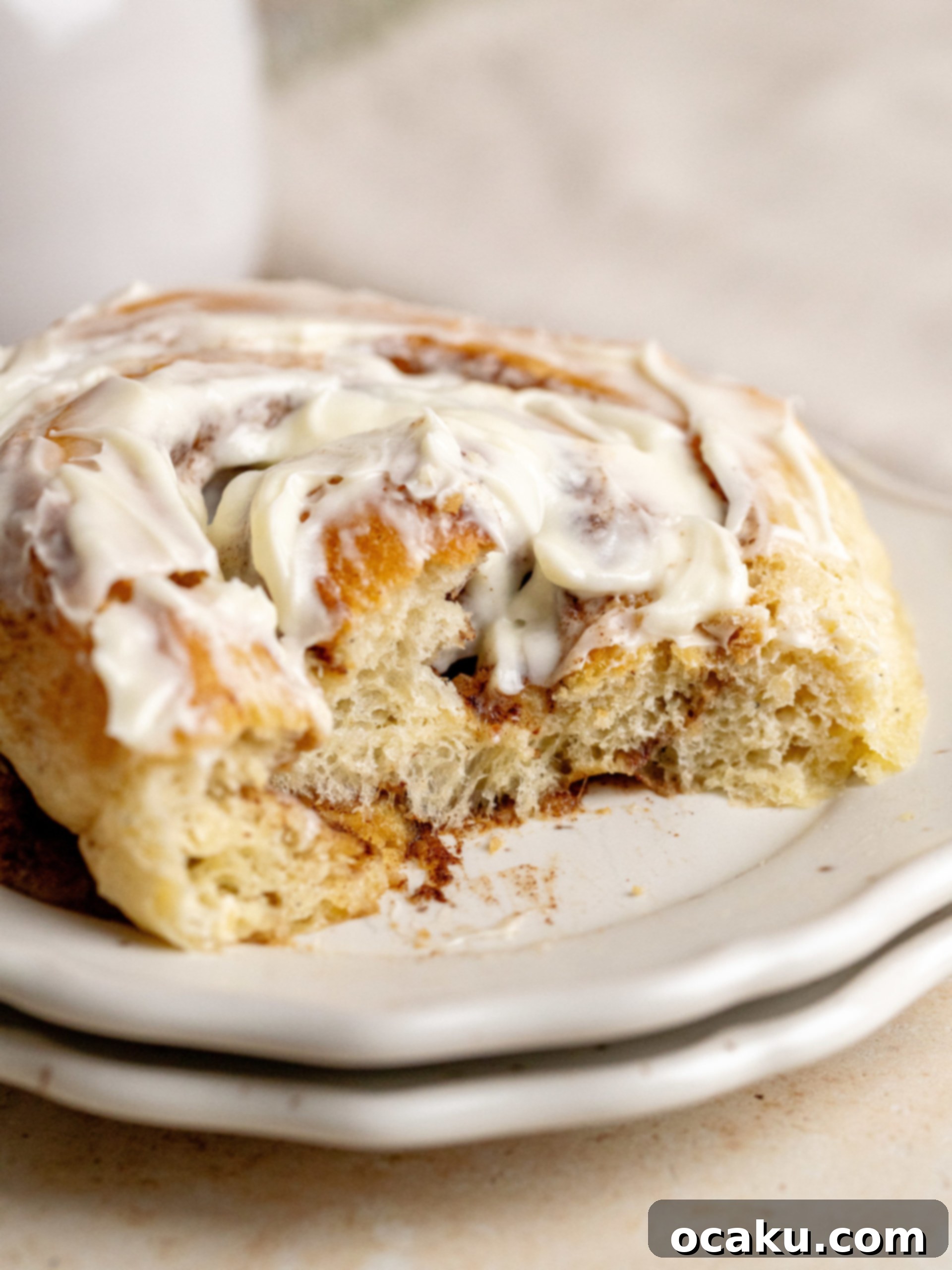 A single giant cinnamon roll, perfectly frosted, on a white plate ready to be enjoyed.